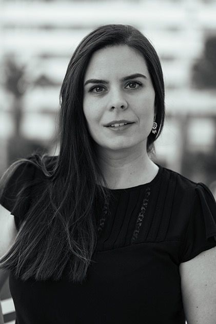 Professional woman with long dark hair wearing black top posing outdoors in black and white portrait.