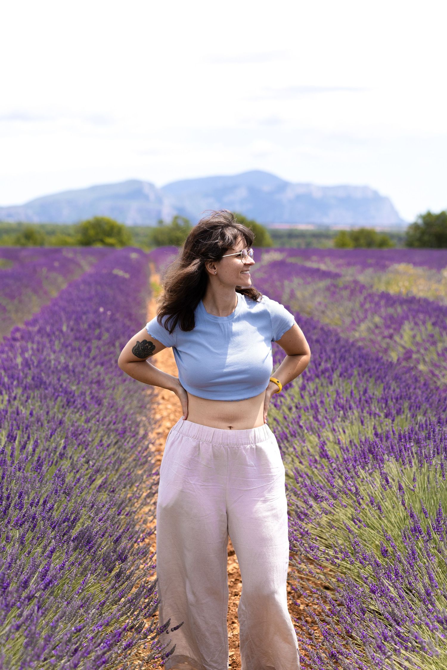 Woman in blue crop top and white pants posing confidently in a vibrant purple lavender field.