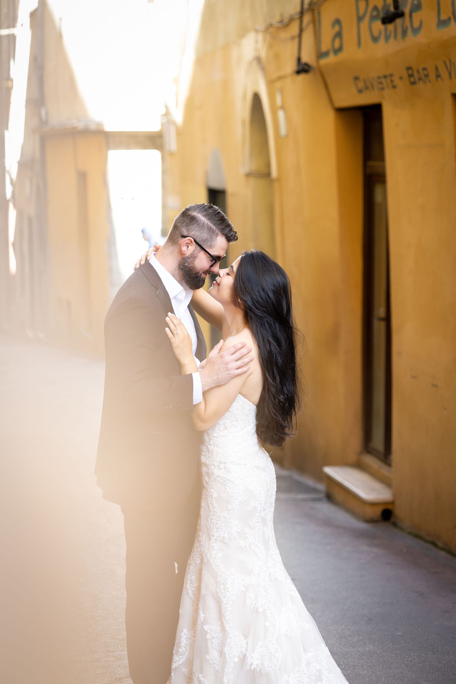 Bride and groom sharing romantic moment in golden sunlit narrow European alley.