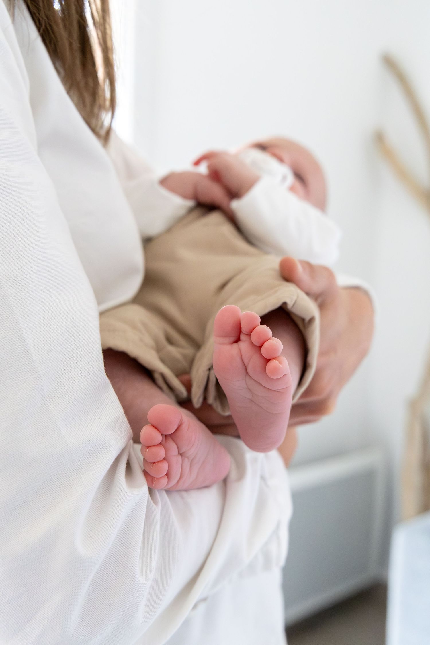 Close-up of tiny newborn baby feet being held by a parent in white clothing.