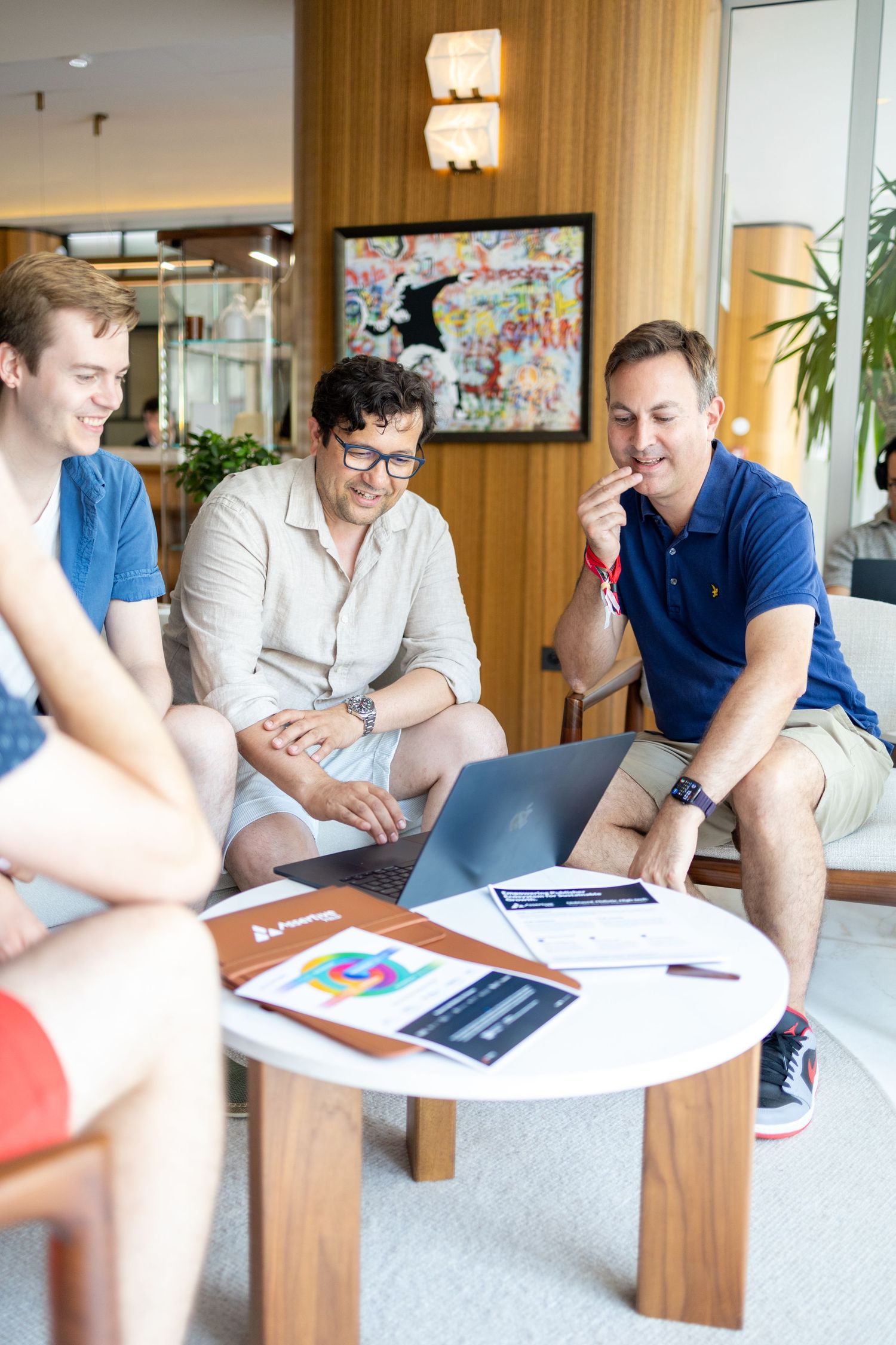 Three young professionals collaborating on a laptop at a modern office lounge with documents on a round table.