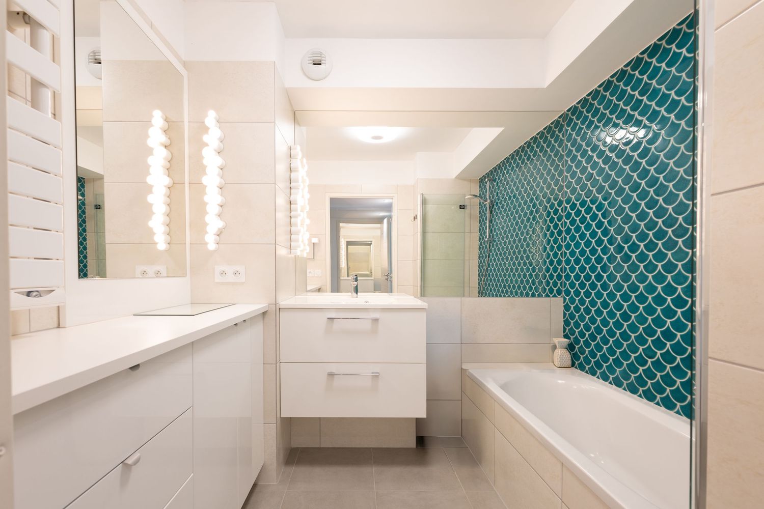Modern white bathroom with teal mosaic tile accent wall, double vanity, and built-in bathtub.