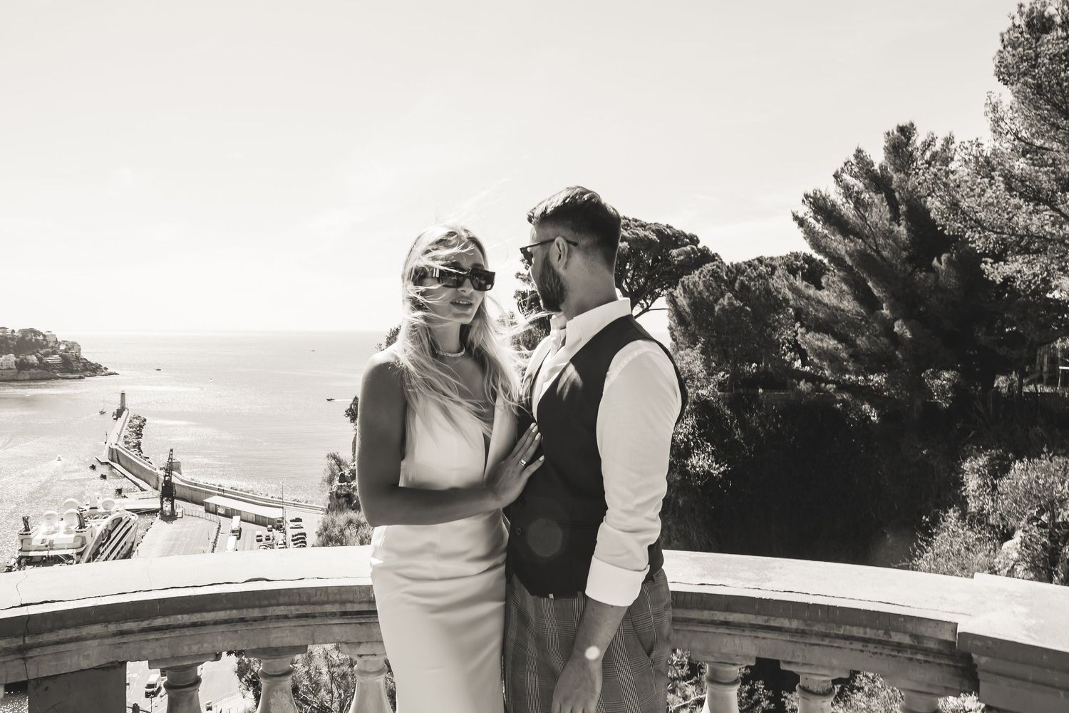 Elegant couple posing on a scenic Mediterranean terrace overlooking the sea in black and white photography.