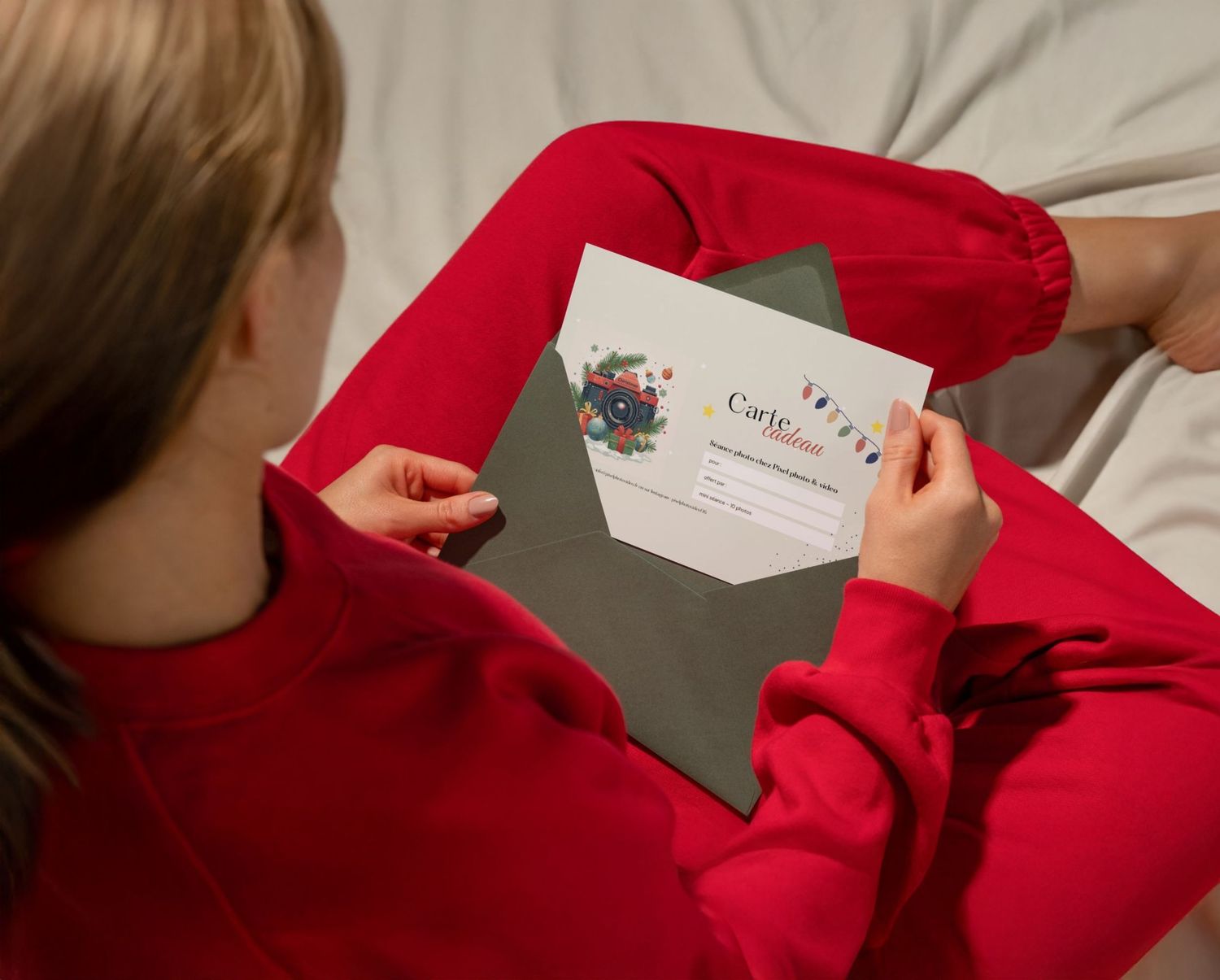 A child in a red sweater holds a festive gift card and gray envelope during the holiday season.