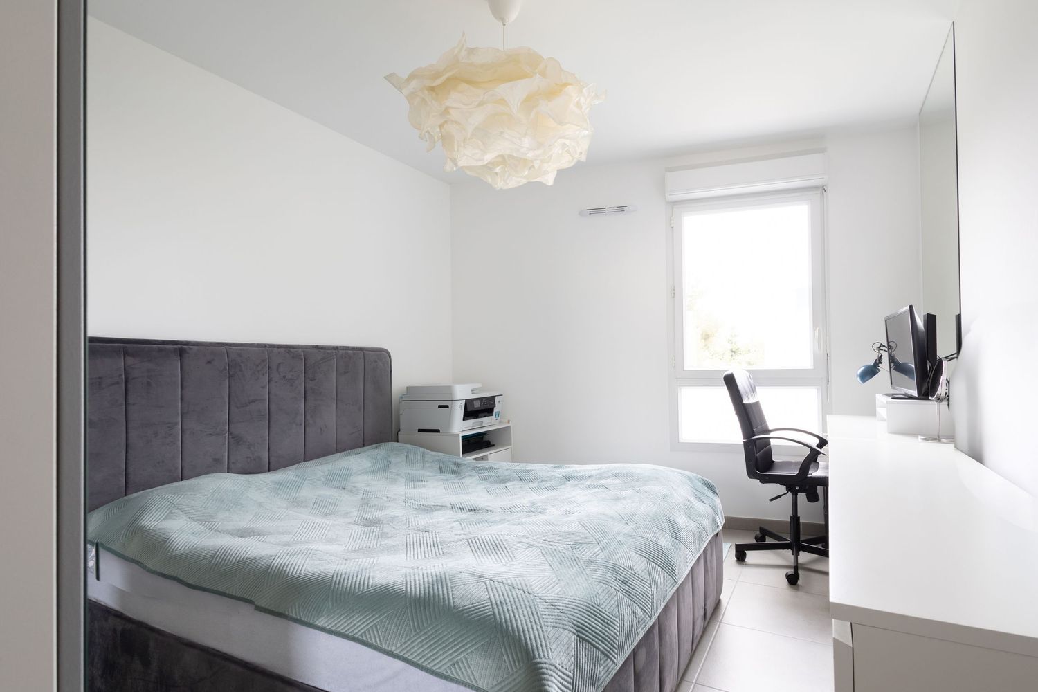 Minimalist bedroom with grey upholstered bed, cloud pendant light, and built-in workspace area.