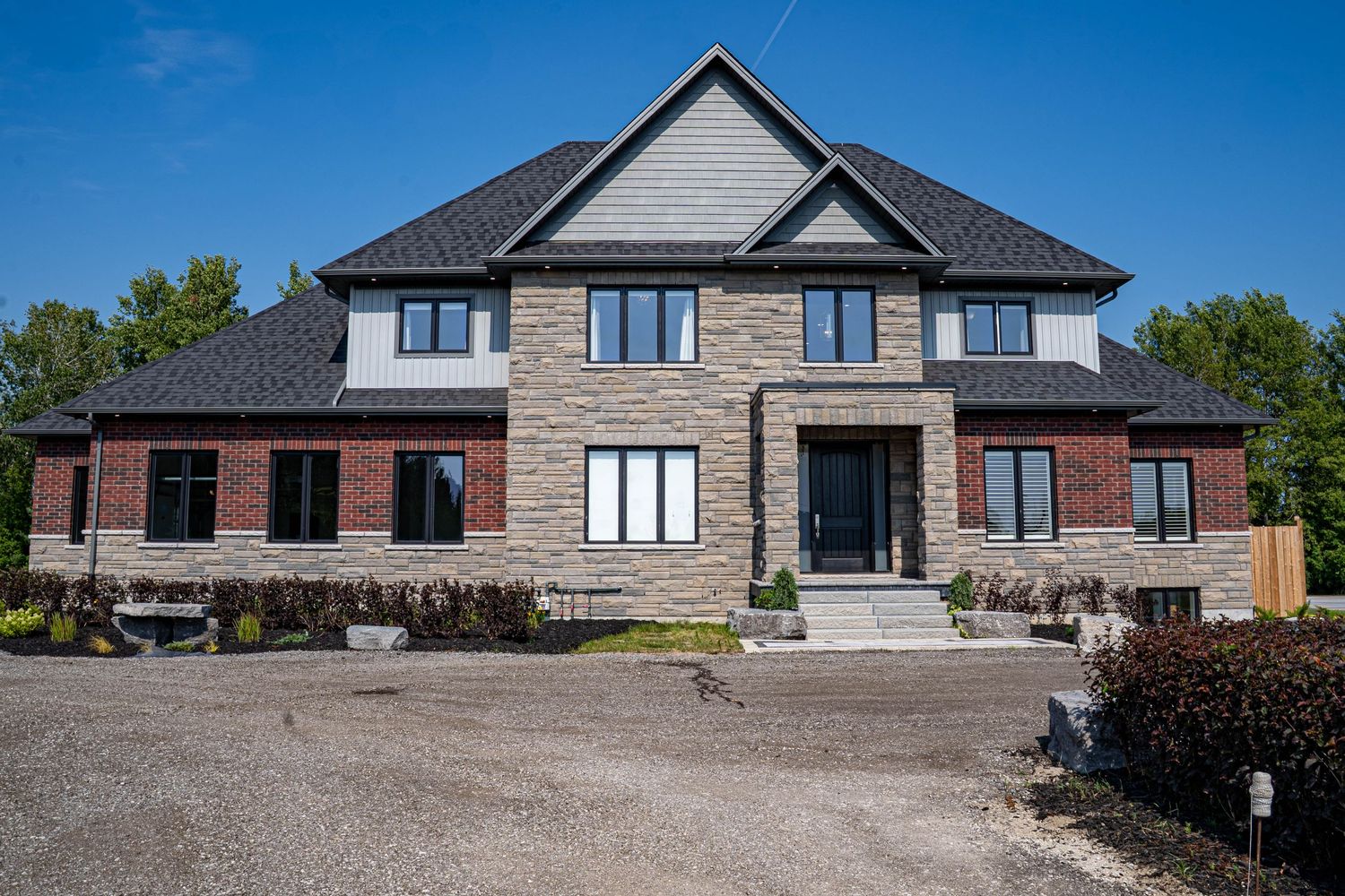 Contemporary stone and brick house with large windows and extended driveway under bright blue sky.