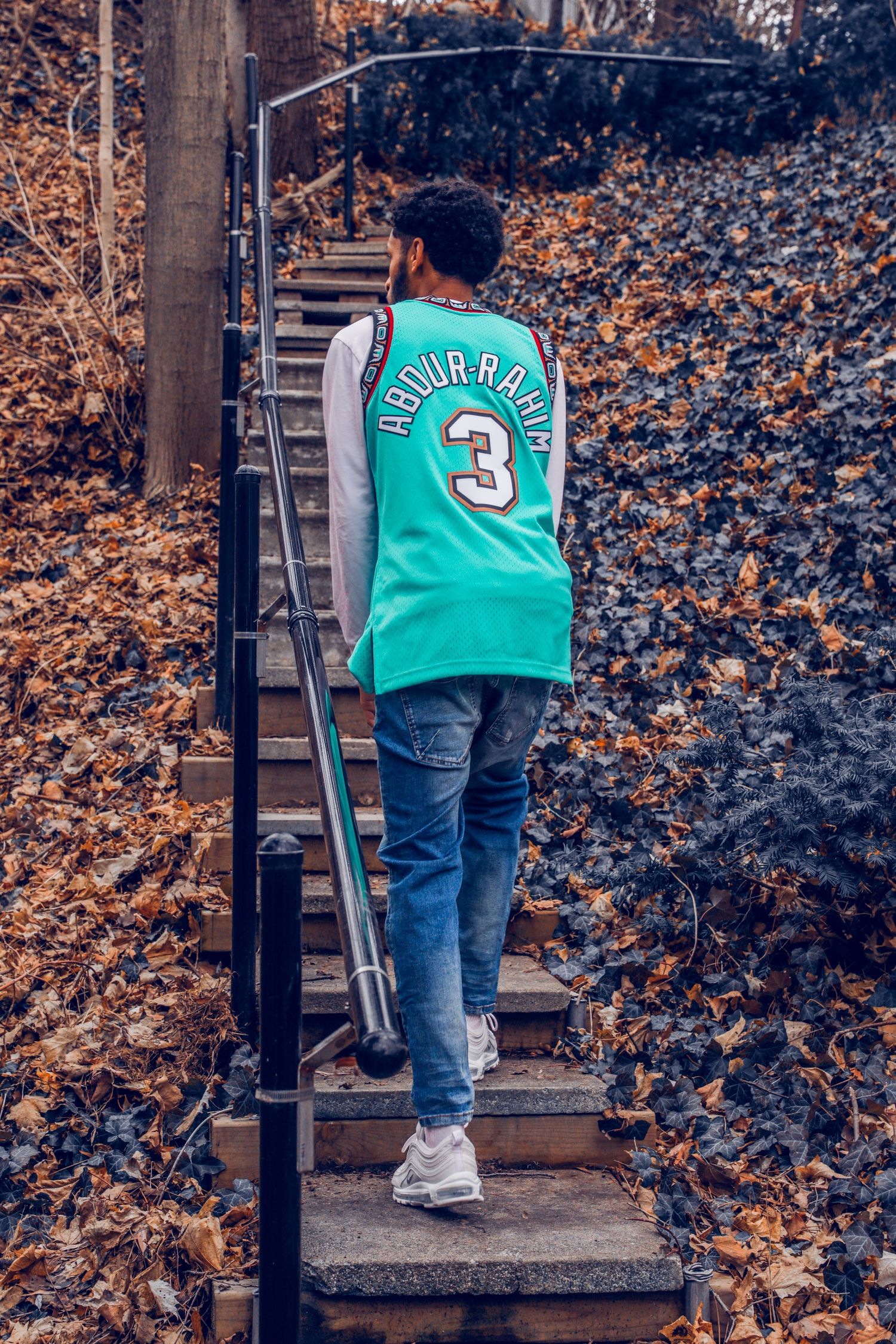 Person wearing teal jersey climbing outdoor stairs surrounded by autumn leaves.