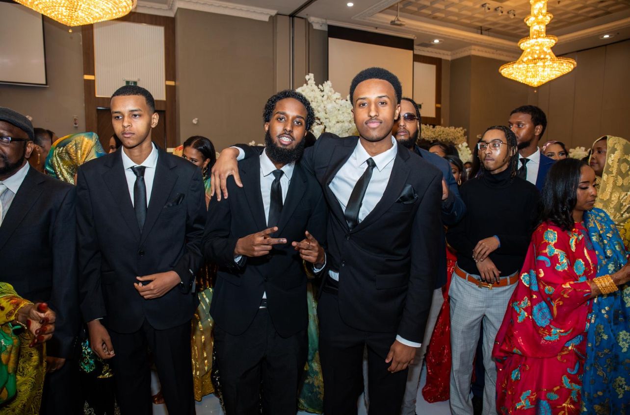 Group of men in formal suits gathering at elegant event with chandeliers.