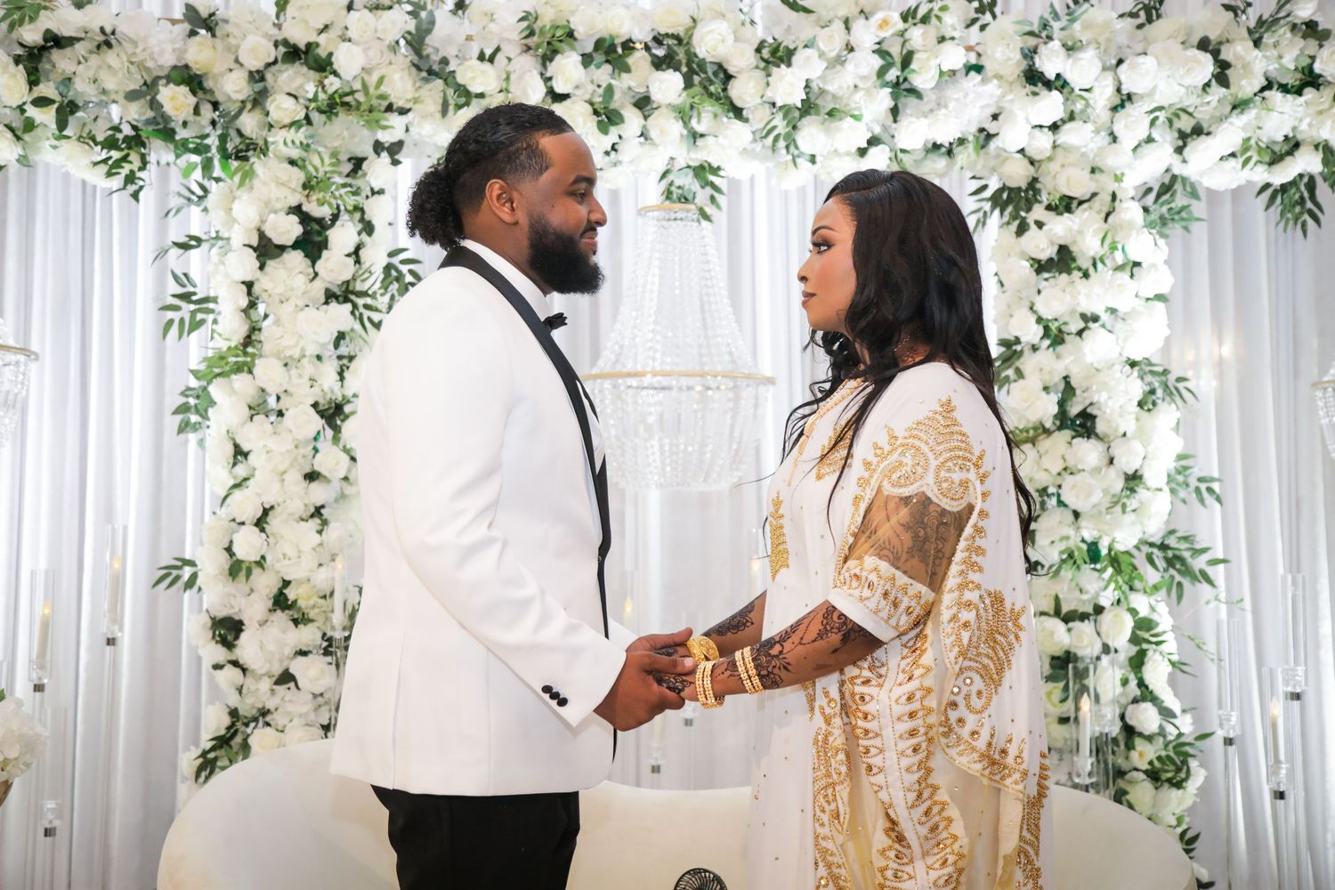 Wedding ceremony moment against white floral backdrop with elegant attire.