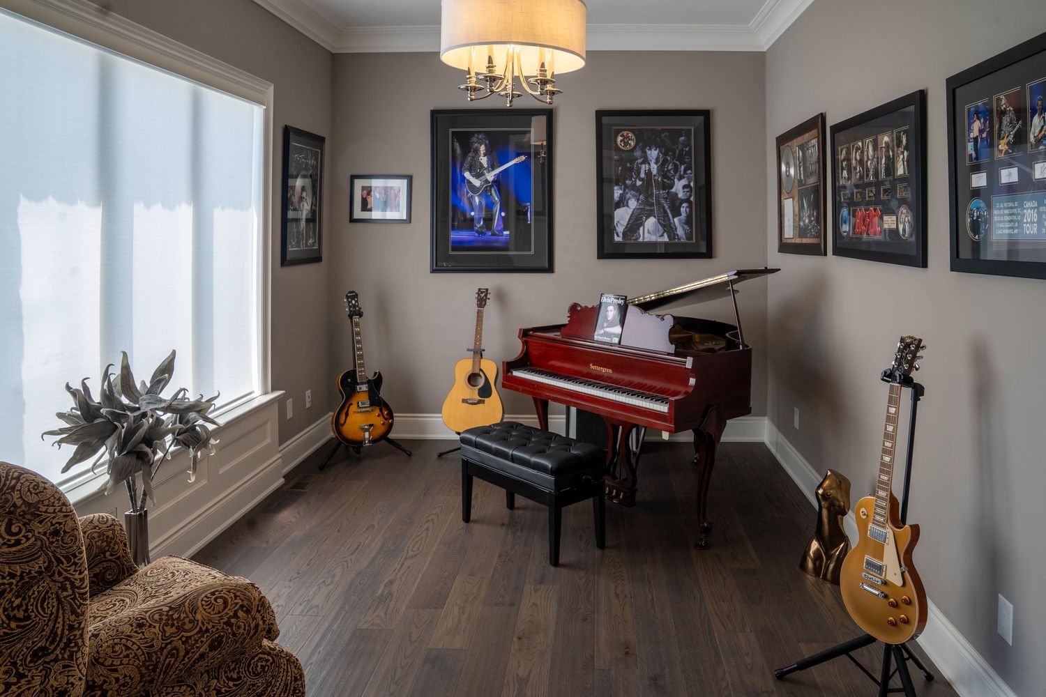 Music room with piano, guitars, and framed memorabilia displayed on gray walls features dark hardwood flooring.