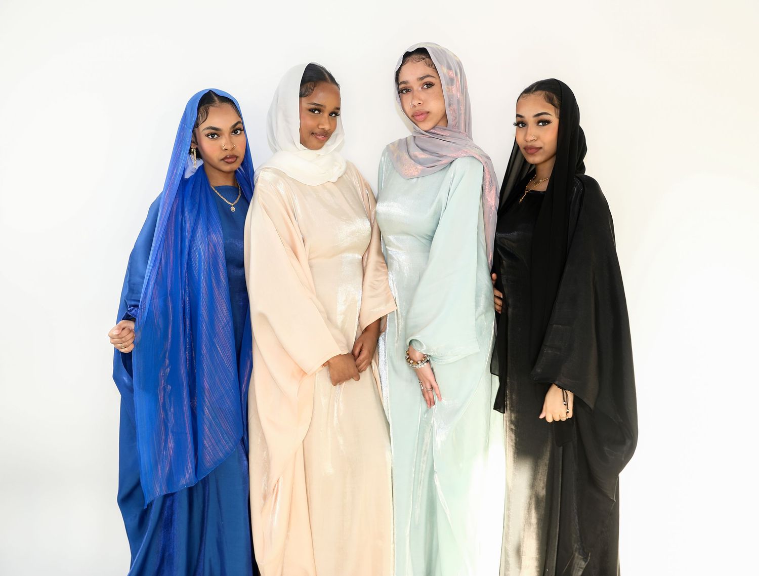 Four women wearing flowing hijabs in different colors against white background.
