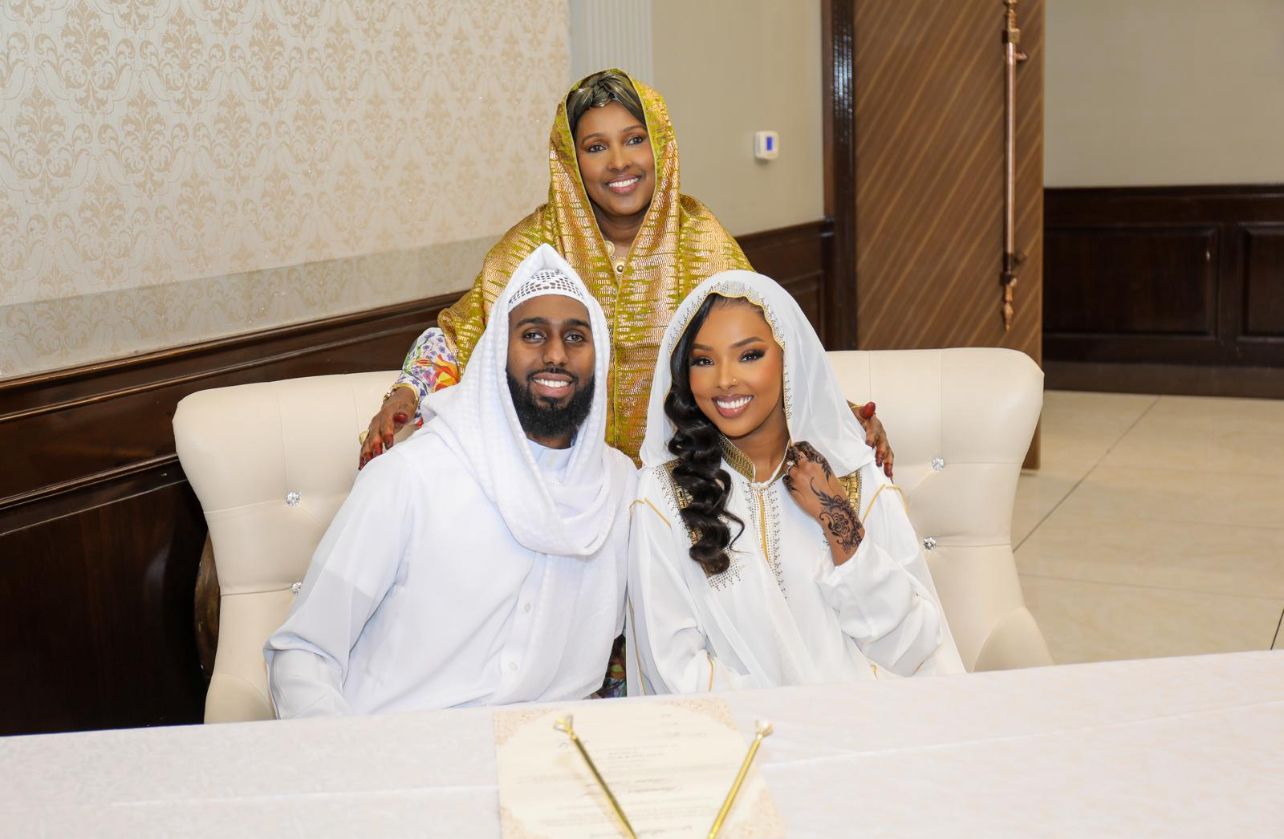 Three people in white traditional dress sitting on couch during celebration.