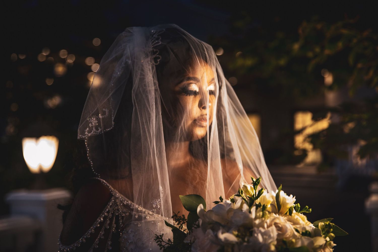 Bride wearing delicate veil holds bouquet during evening outdoor portrait session.