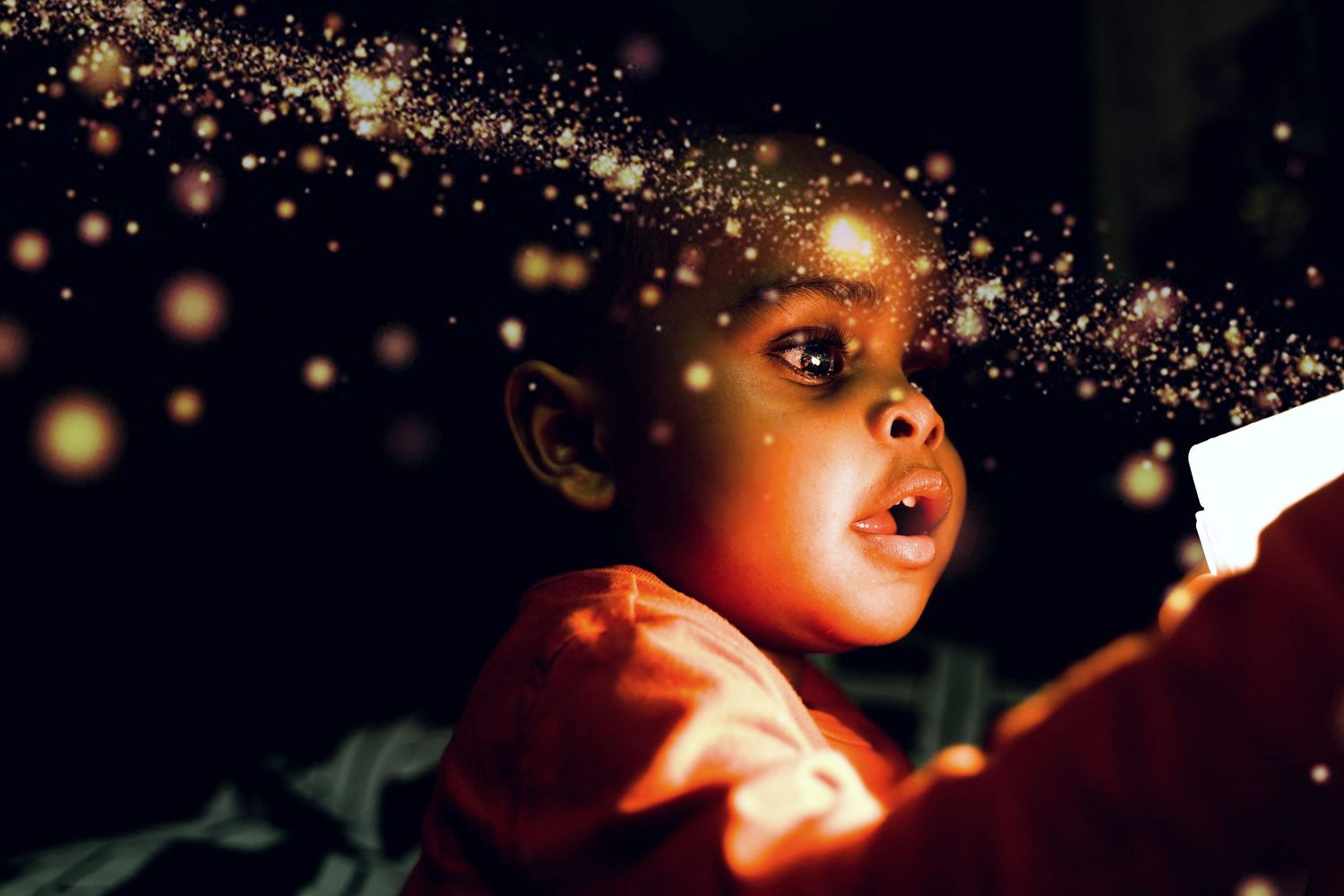 Child gazing upward with magical golden sparkles and bokeh lights creating dreamy atmosphere.