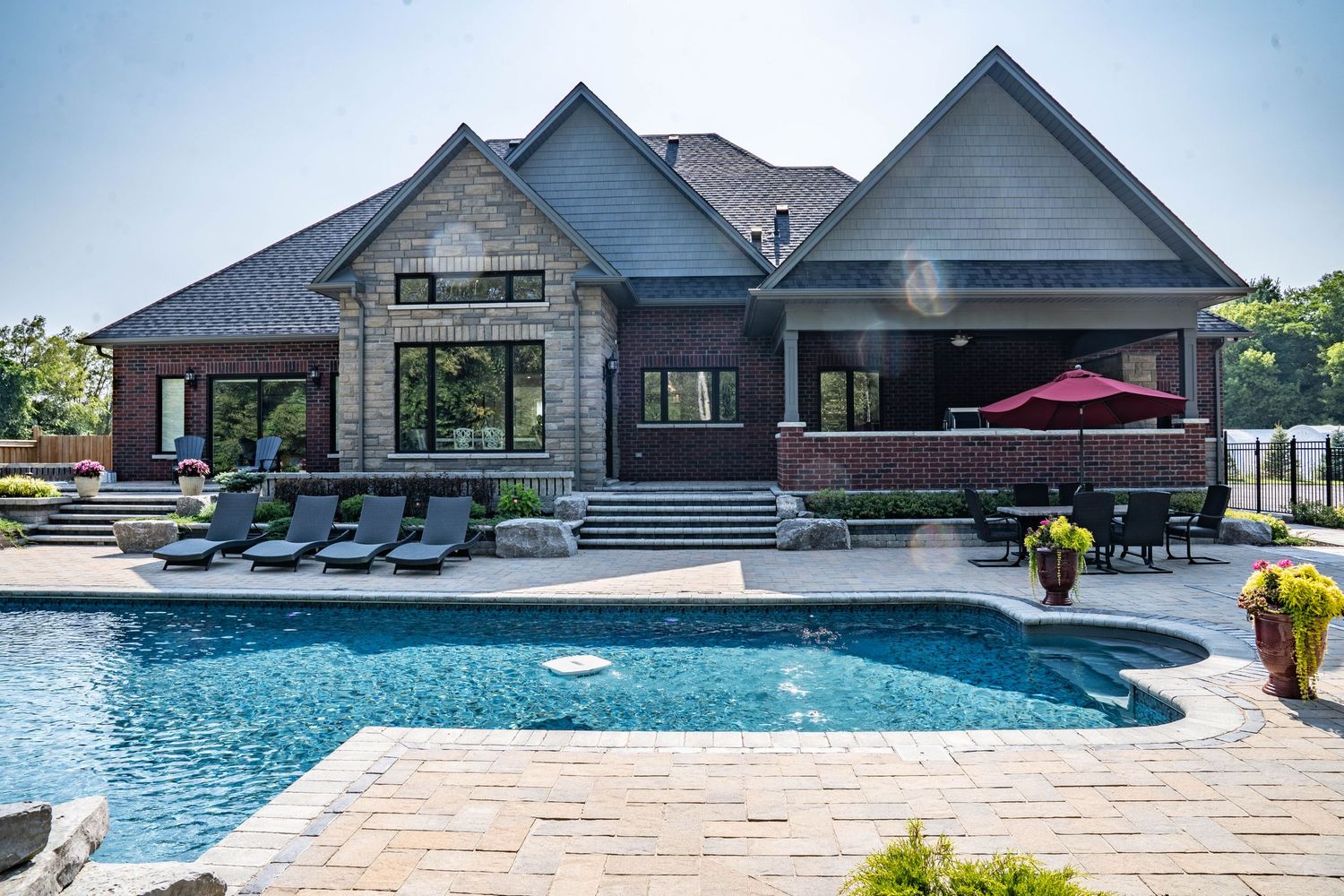 Luxurious backyard featuring an L-shaped swimming pool with stone patio and lounge chairs beside modern house.
