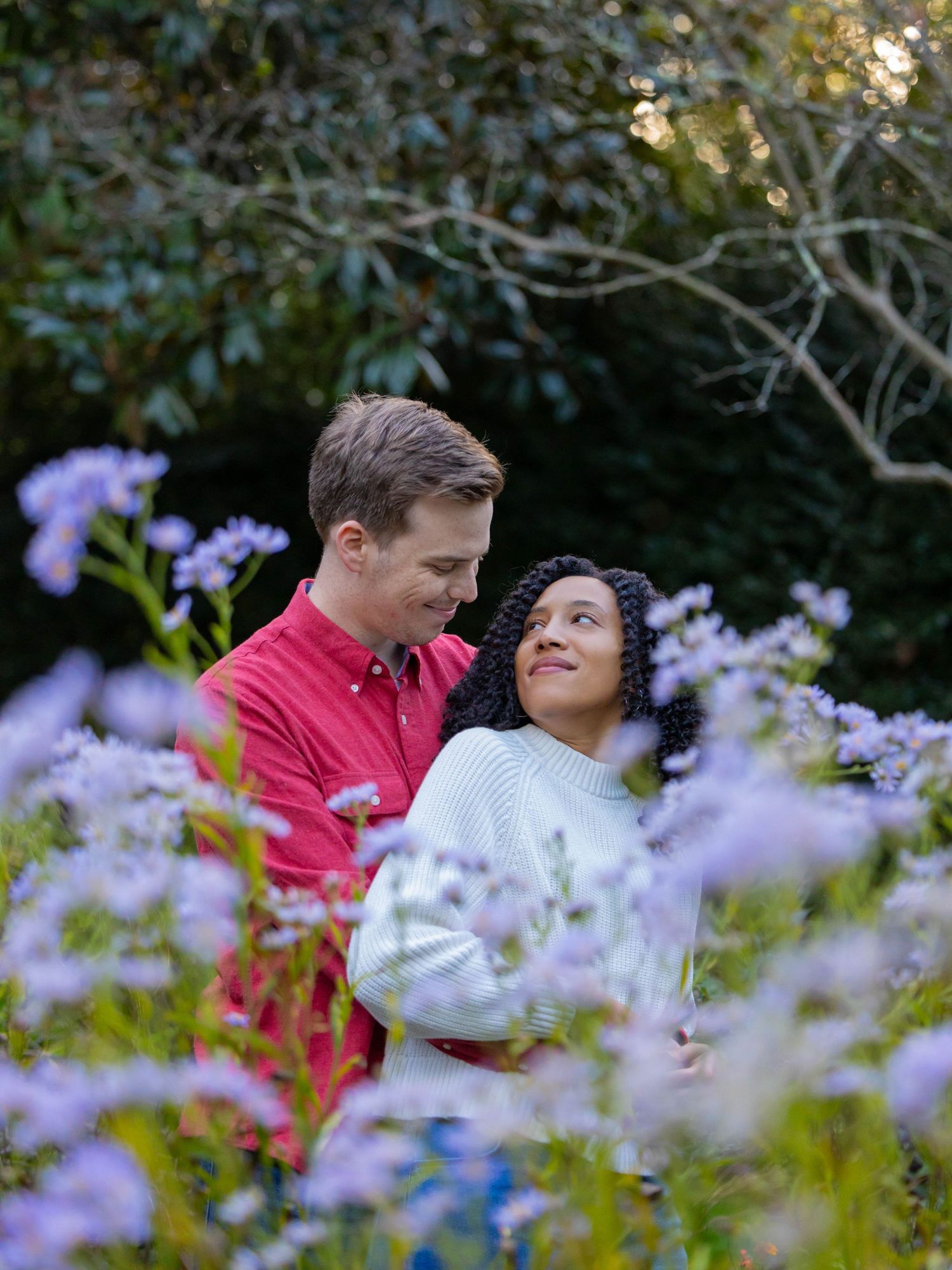 A couple shares an intimate moment among blooming purple flowers in a garden setting.