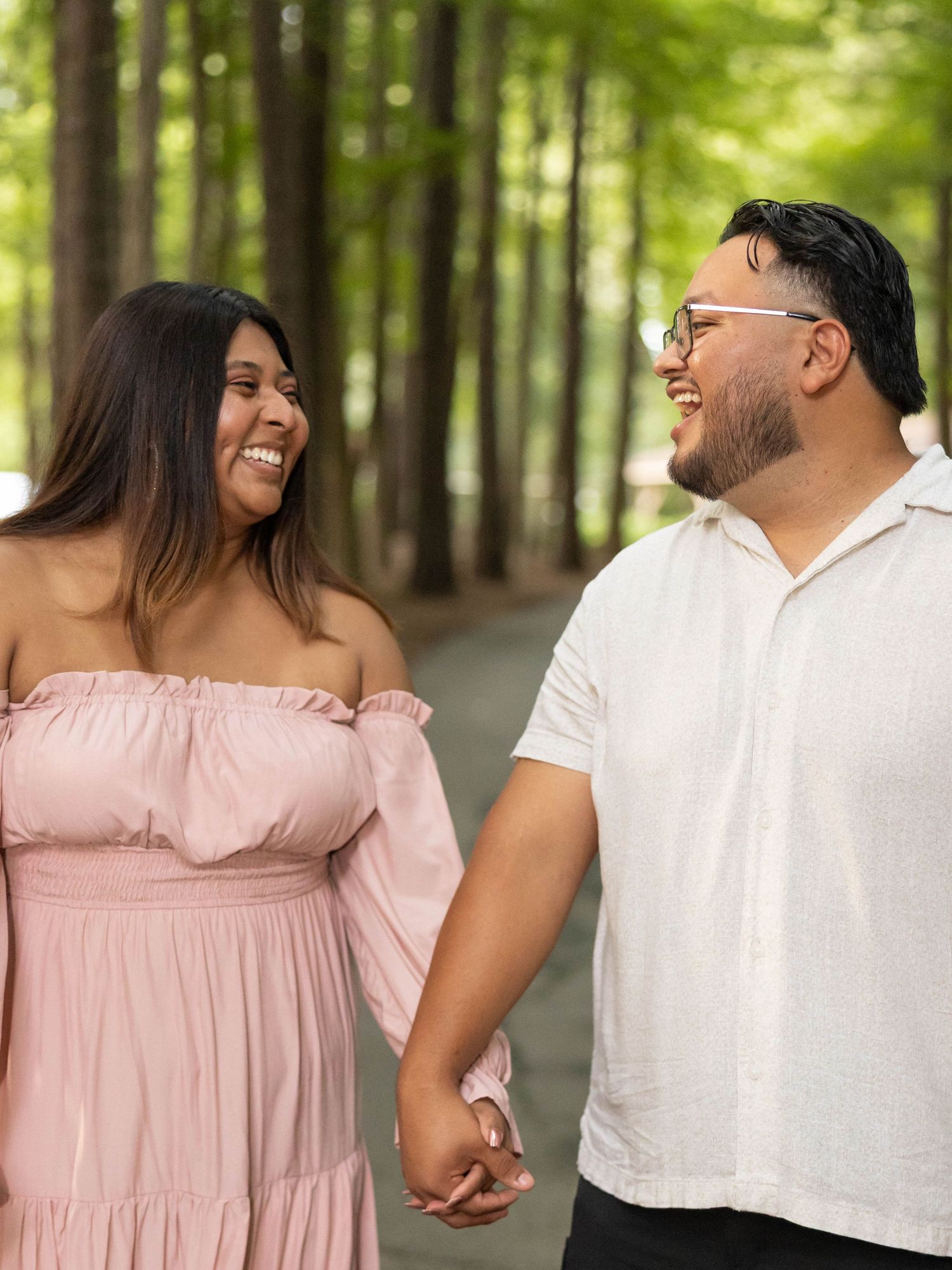 A happy couple shares a joyful moment together while holding hands on a tree-lined path in summer.