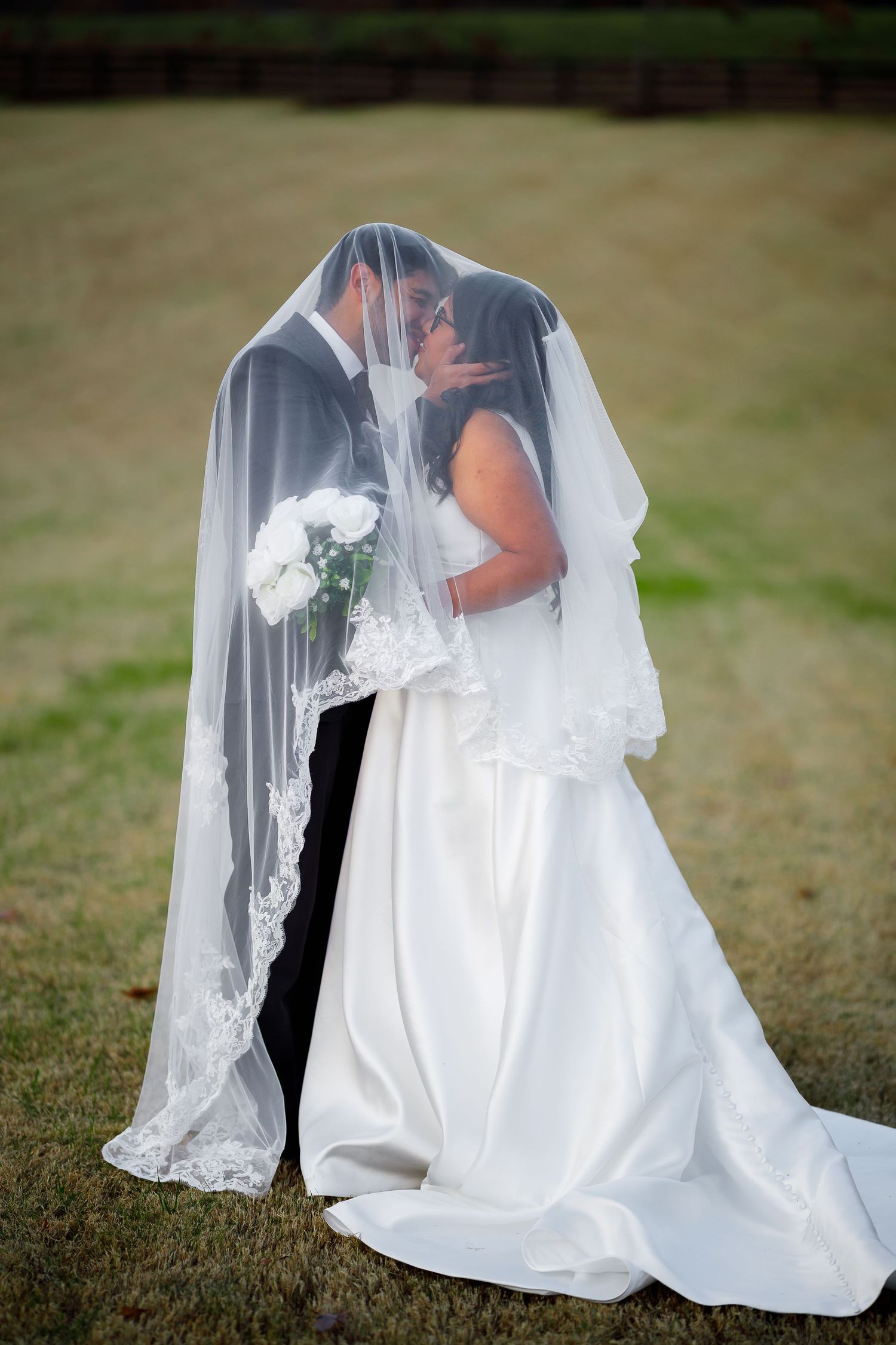 A romantic wedding photo series showing a couple embracing under a flowing white veil in an outdoor garden setting.