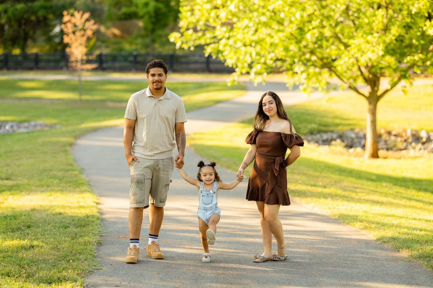 Happy family of three strolling together on a sunny park path surrounded by green trees.
