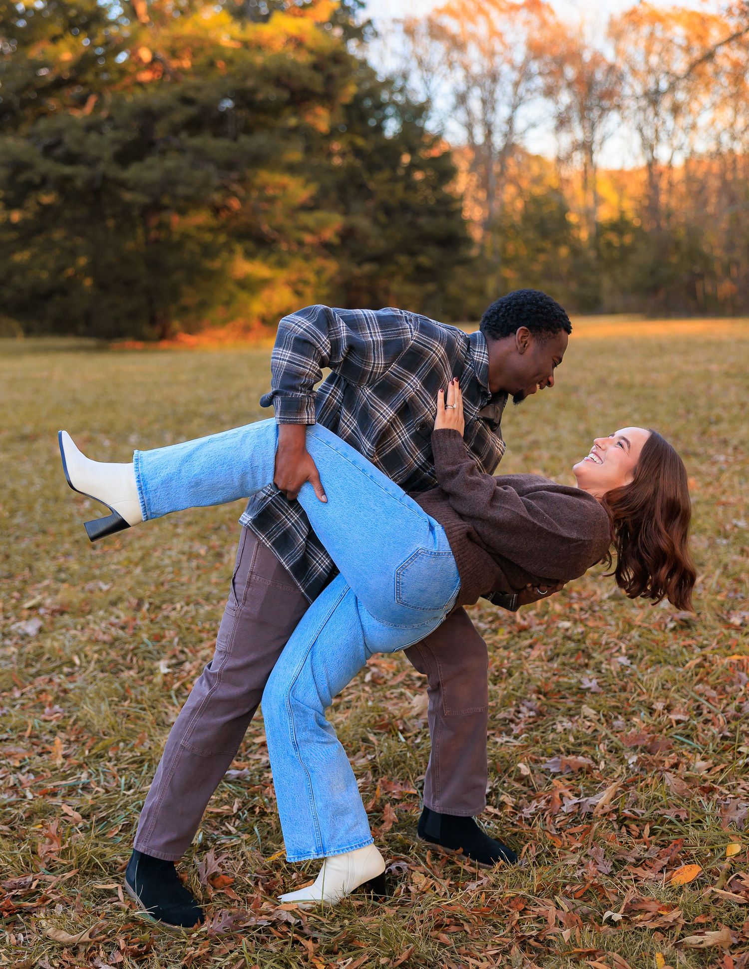 A couple shares a romantic dance pose surrounded by autumn foliage in a park setting during golden hour.