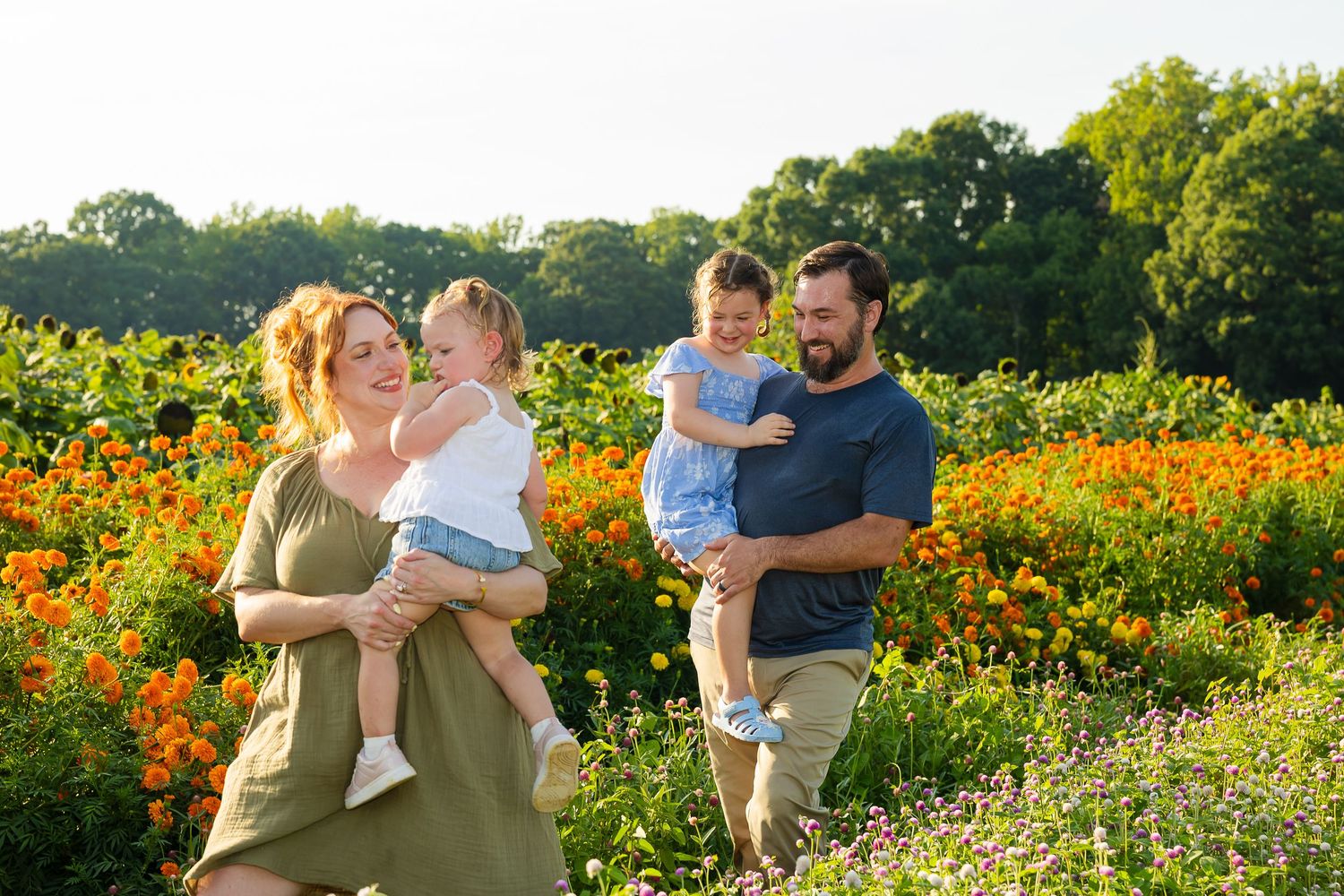 Family of four with two toddlers posing in a vibrant wildflower field on a sunny day.