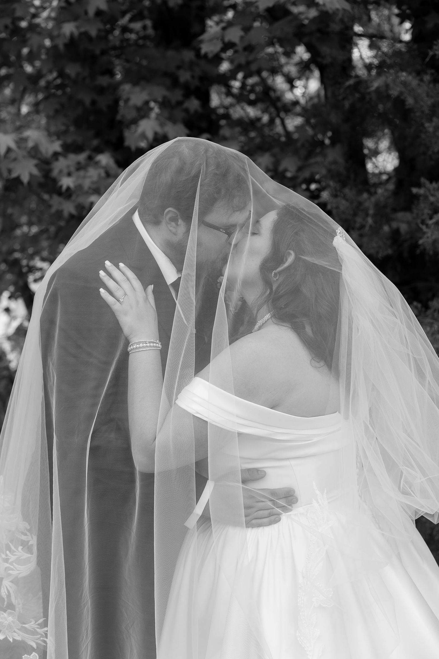 Black and white photo of bride and groom sharing a kiss hidden beneath a flowing wedding veil.