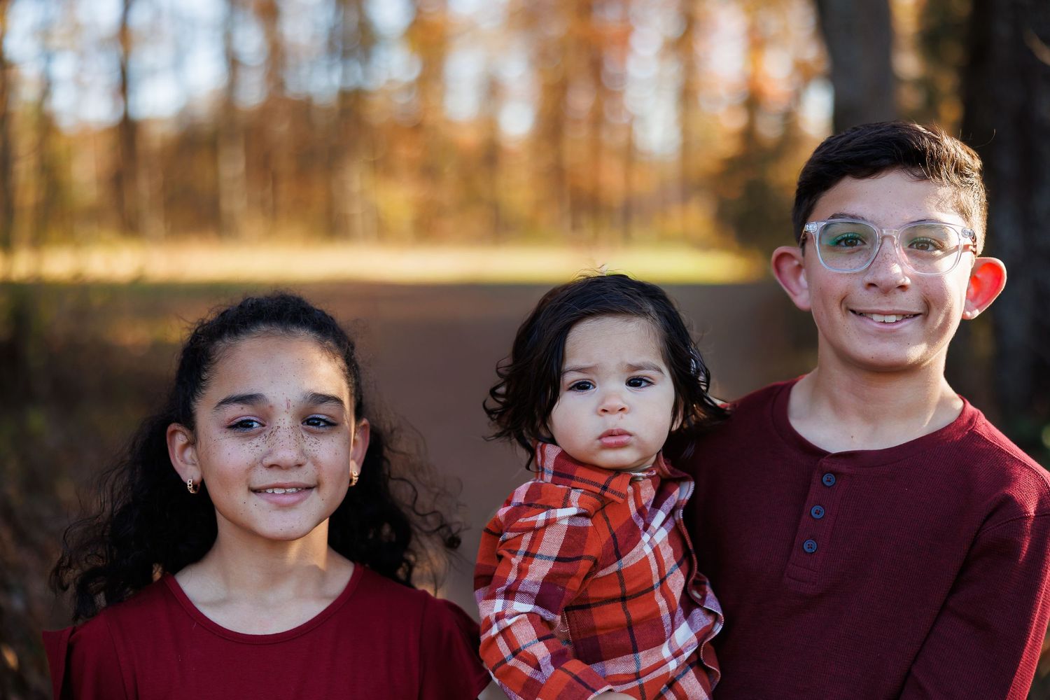 A group of children wearing coordinated red and black outfits pose together for a holiday photo outdoors in autumn.