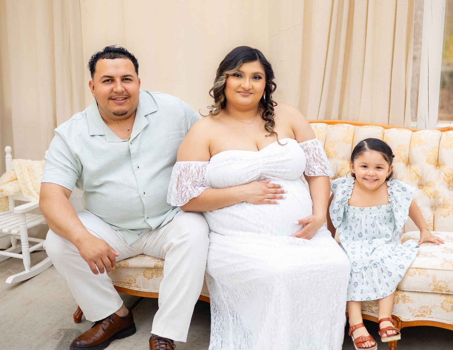 Family poses together on elegant cream sofa wearing coordinated white and light blue outfits for formal portrait session.