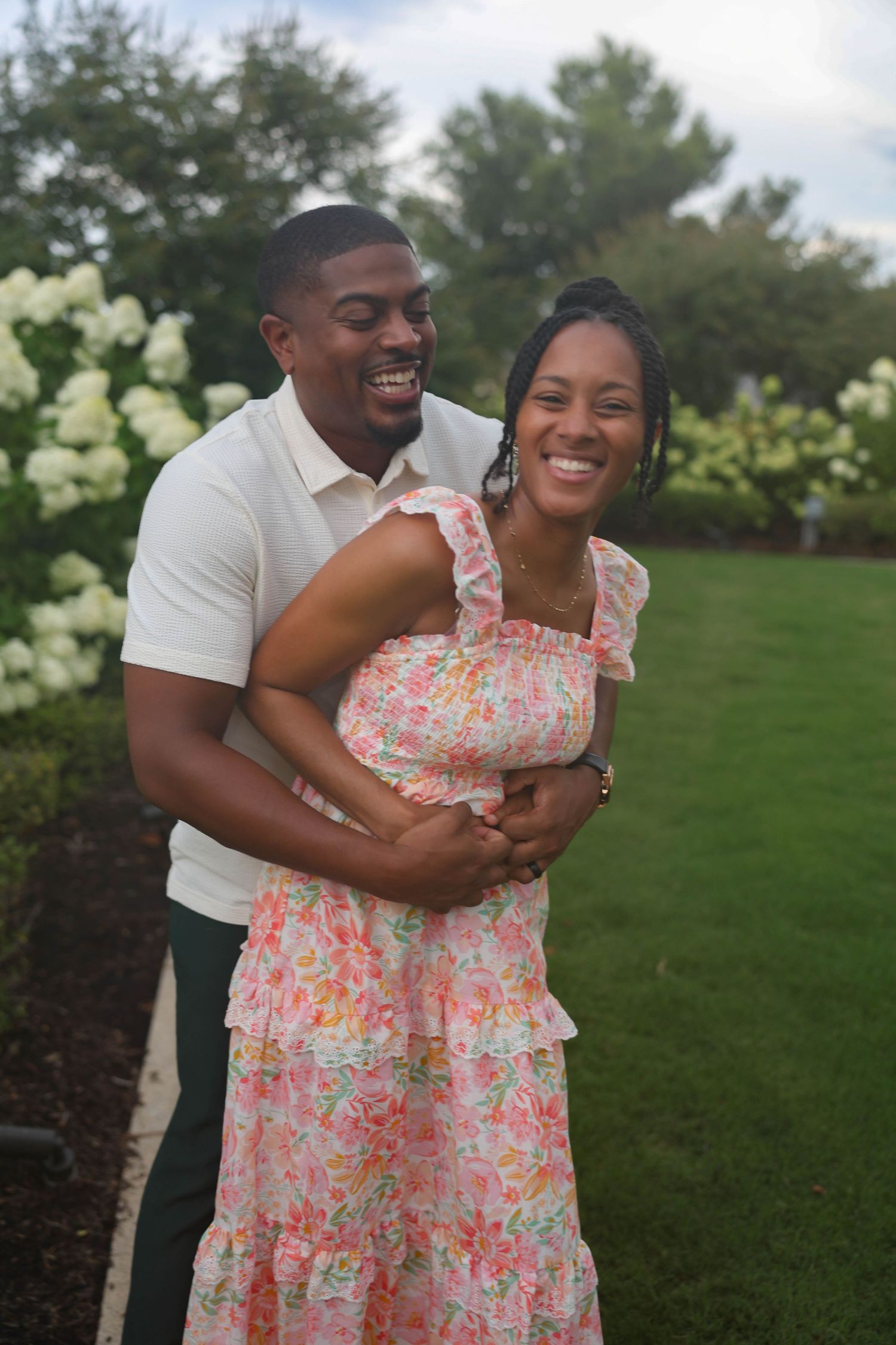 A couple shares a joyful embrace in a garden setting with white hydrangea bushes in the background.