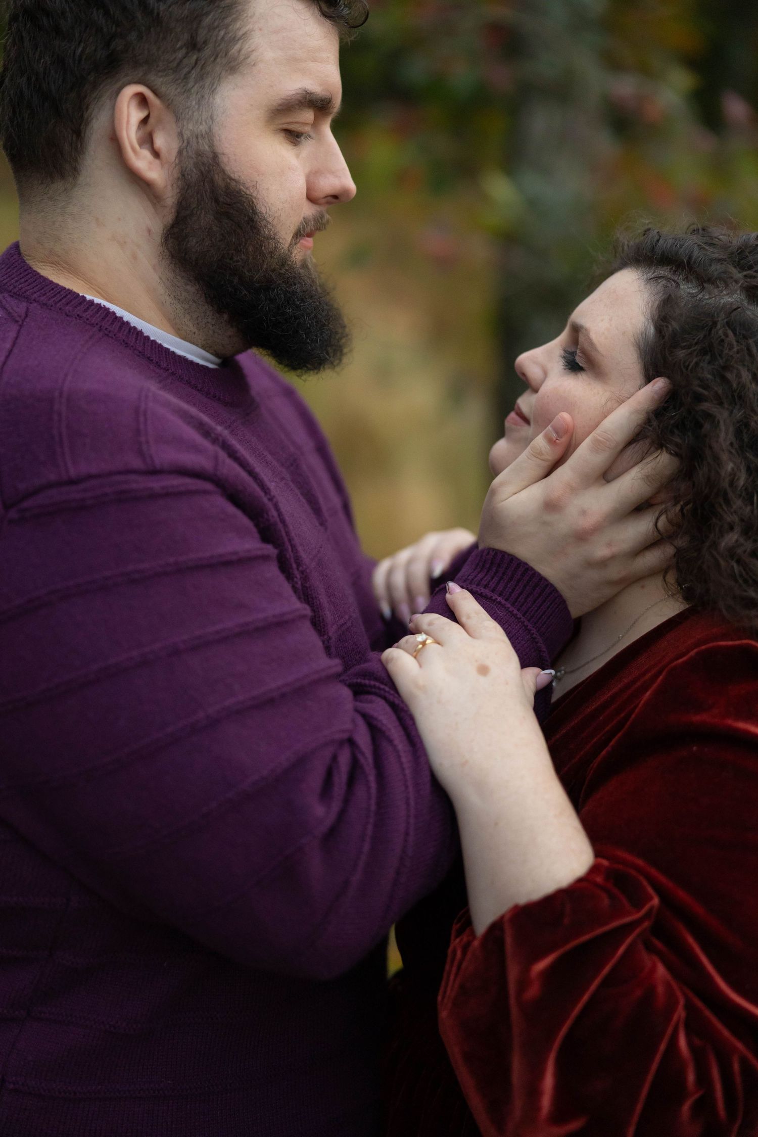 A romantic couple embraces outdoors wearing burgundy and purple clothing during an autumn photoshoot.