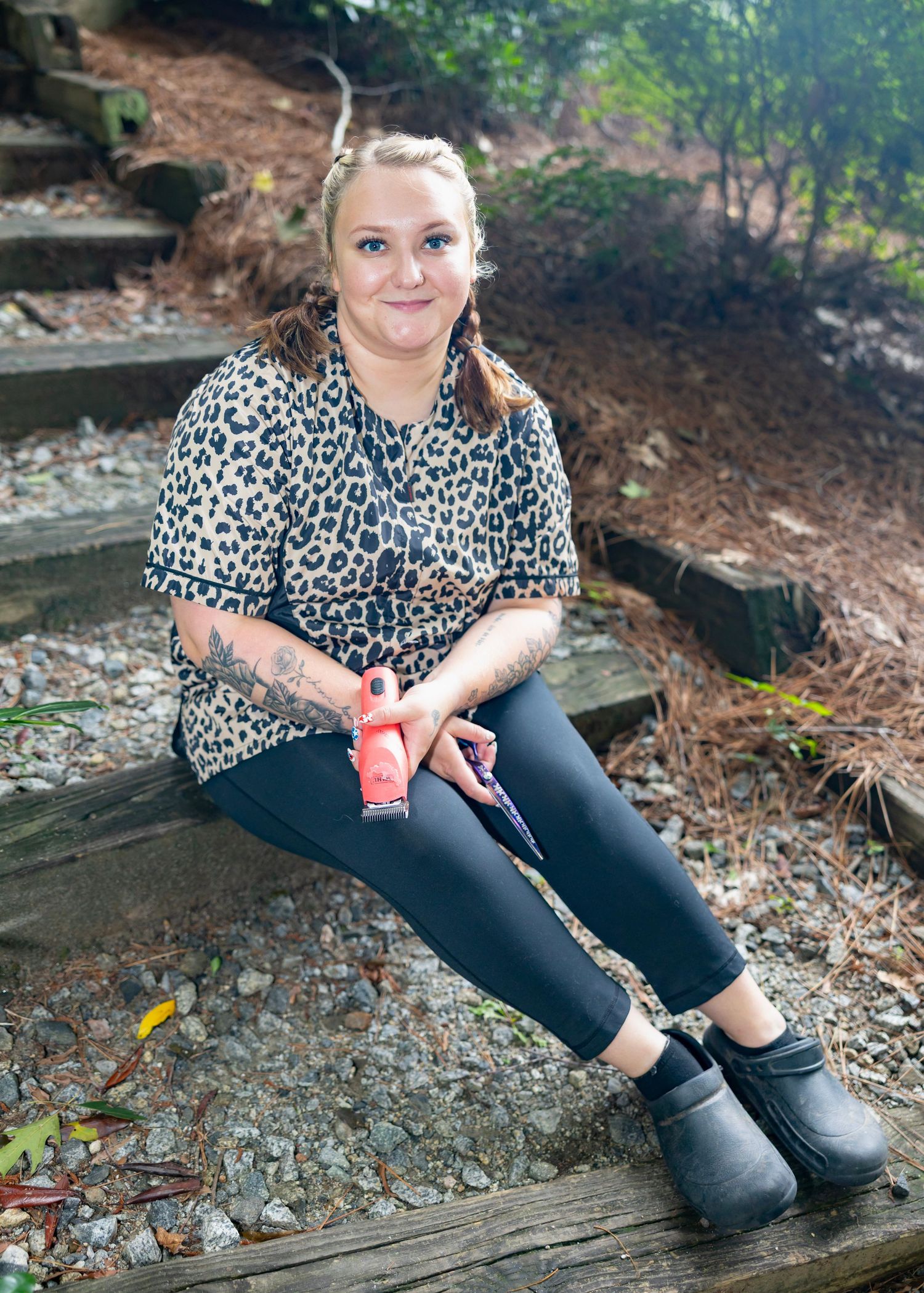 A person in a leopard print top and black leggings sits on wooden steps outdoors holding a beverage.