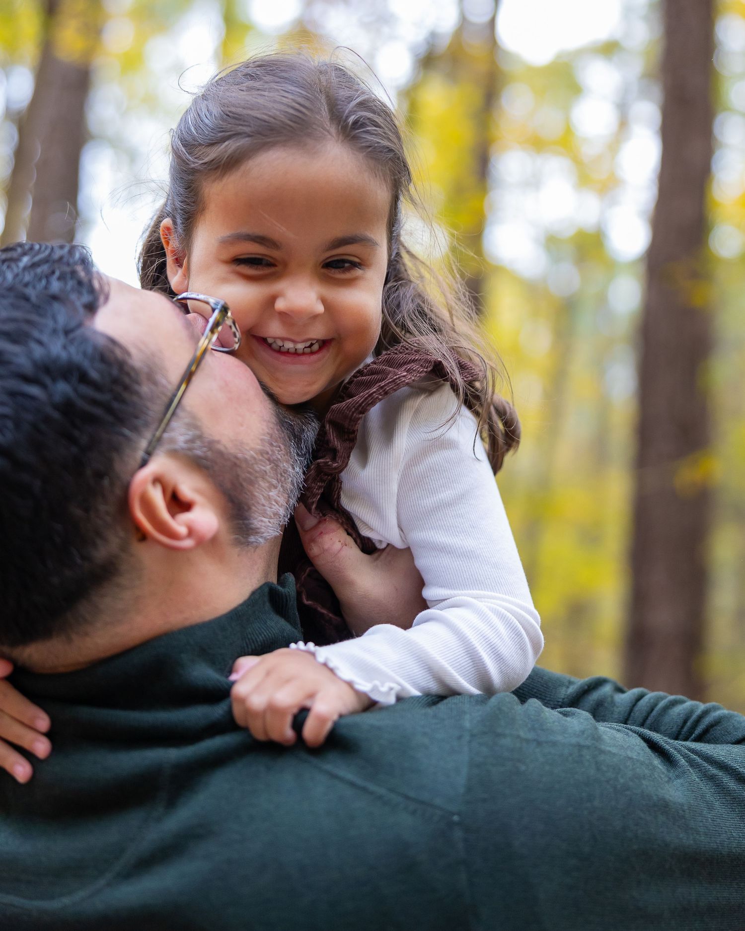 A sweet moment of joy and laughter shared between parent and child amid fall foliage in the forest.