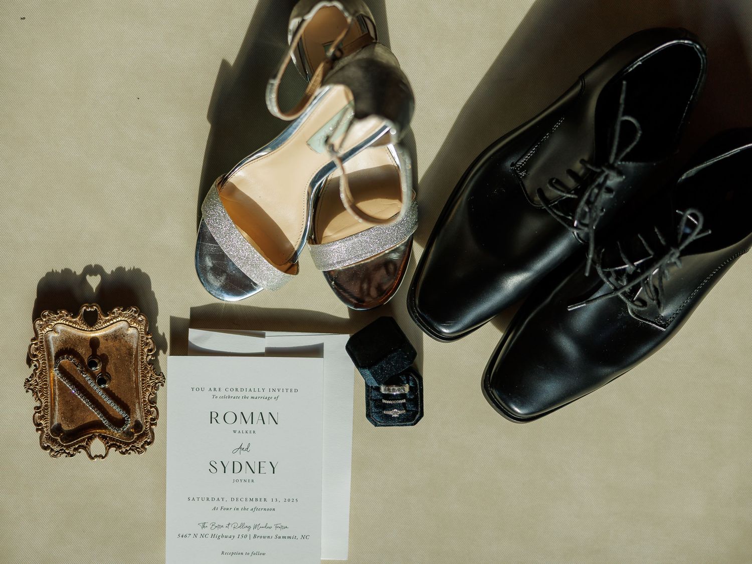 Elegant wedding details including formal black dress shoes, invitation, and vintage accessories arranged on a light surface.