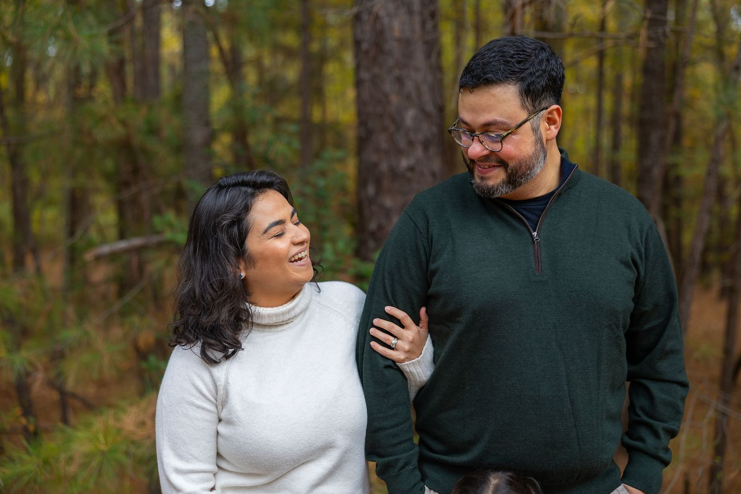 A couple in autumn attire shares a candid moment together while walking through a wooded forest setting.