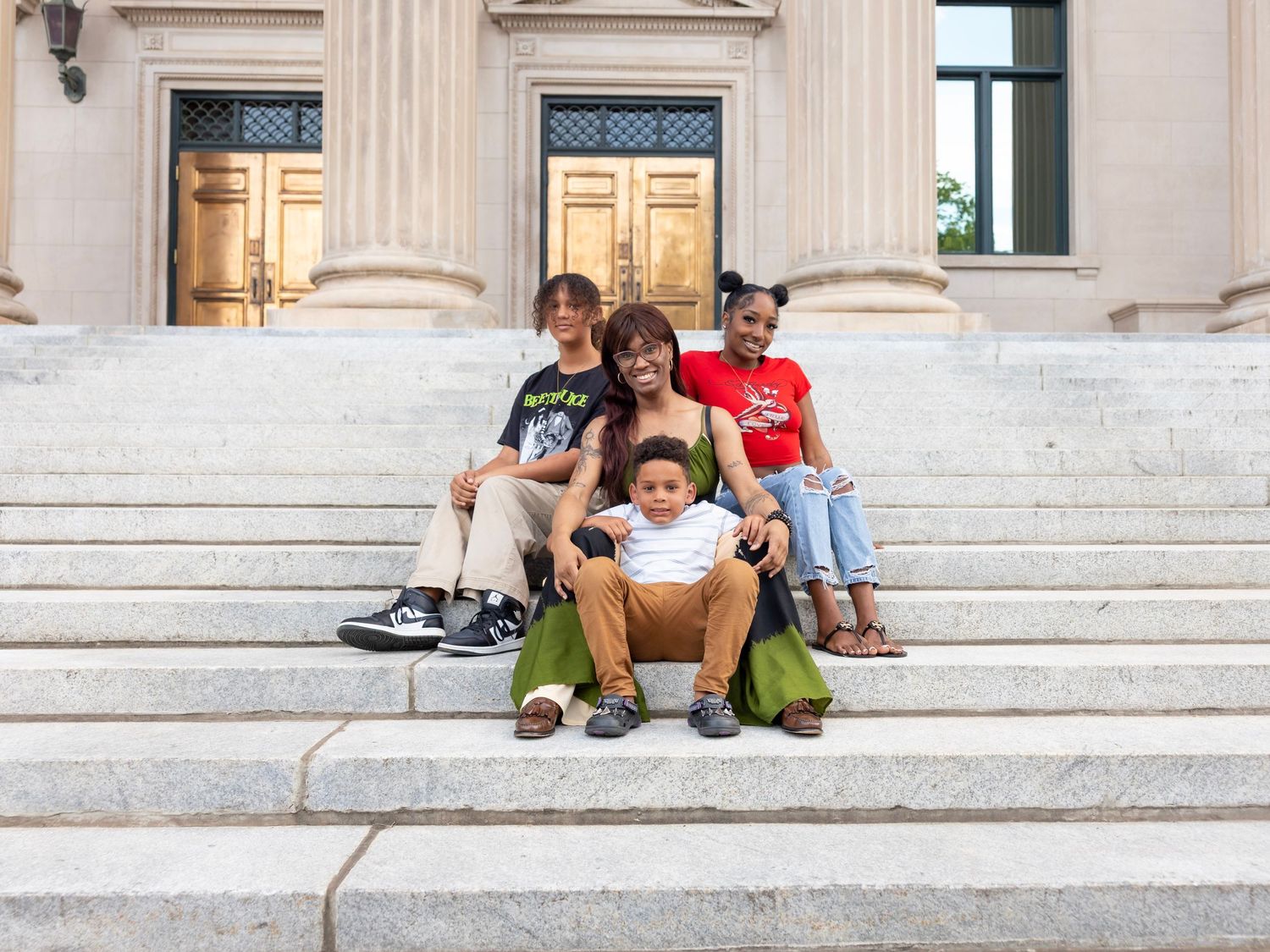 People resting on white stone steps outside a classical building during a summer day.