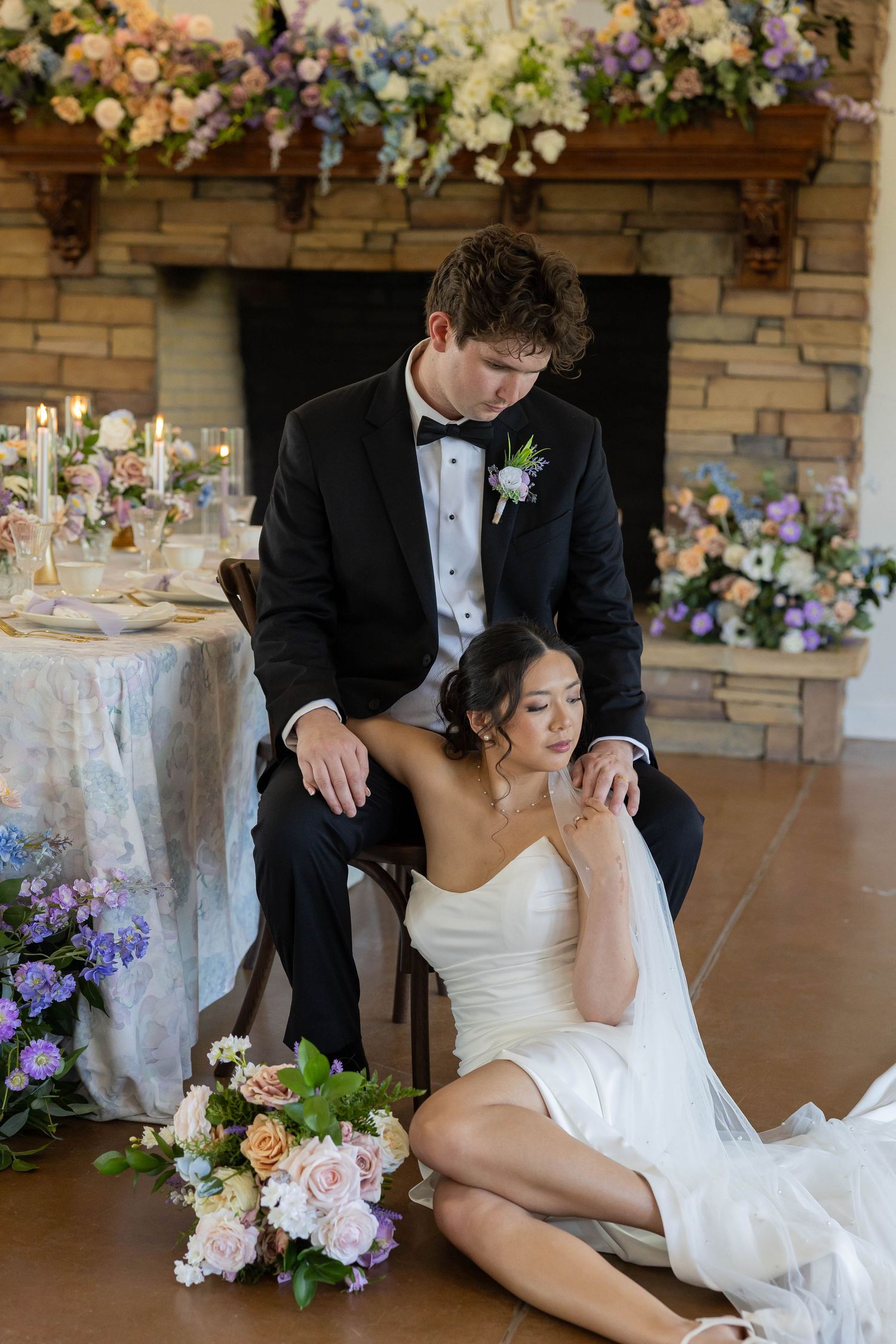 A wedding couple poses together in an elegant indoor venue decorated with floral arrangements and stone walls.
