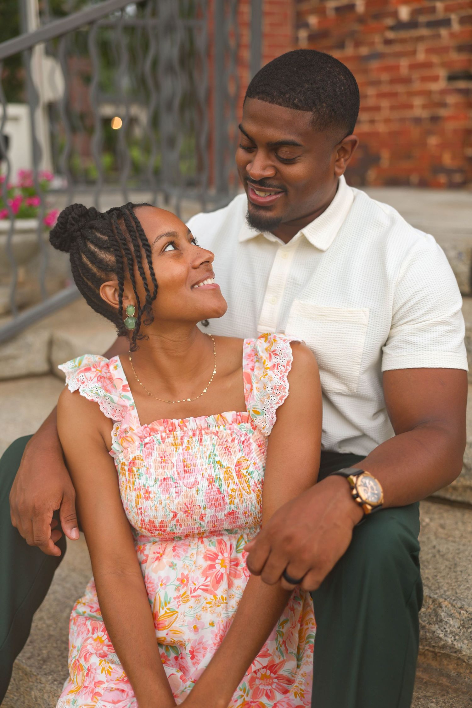 A happy couple shares a romantic moment outdoors, with the woman wearing a floral dress and the man in a white polo.