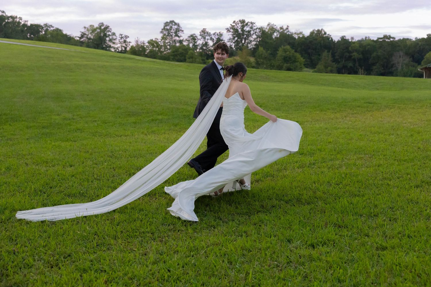 A flowing white dress billows dramatically across a lush green field on an overcast day.