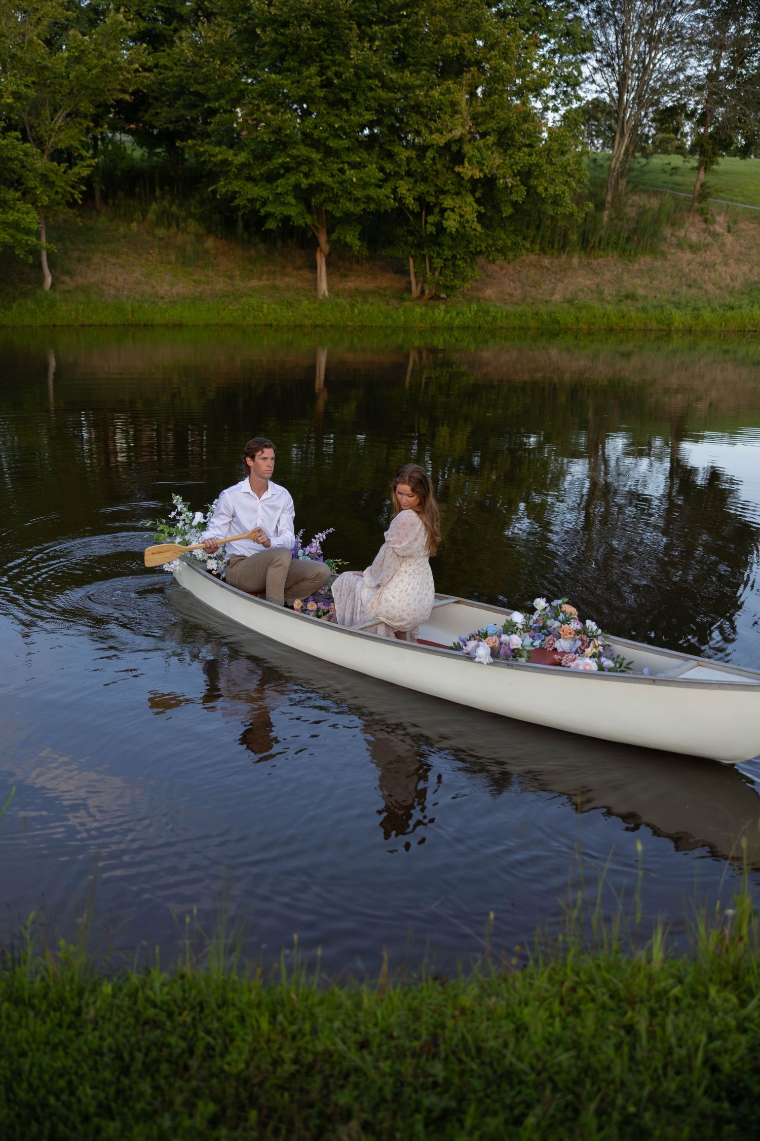 A white canoe floats peacefully on a tranquil pond surrounded by lush greenery at dusk.