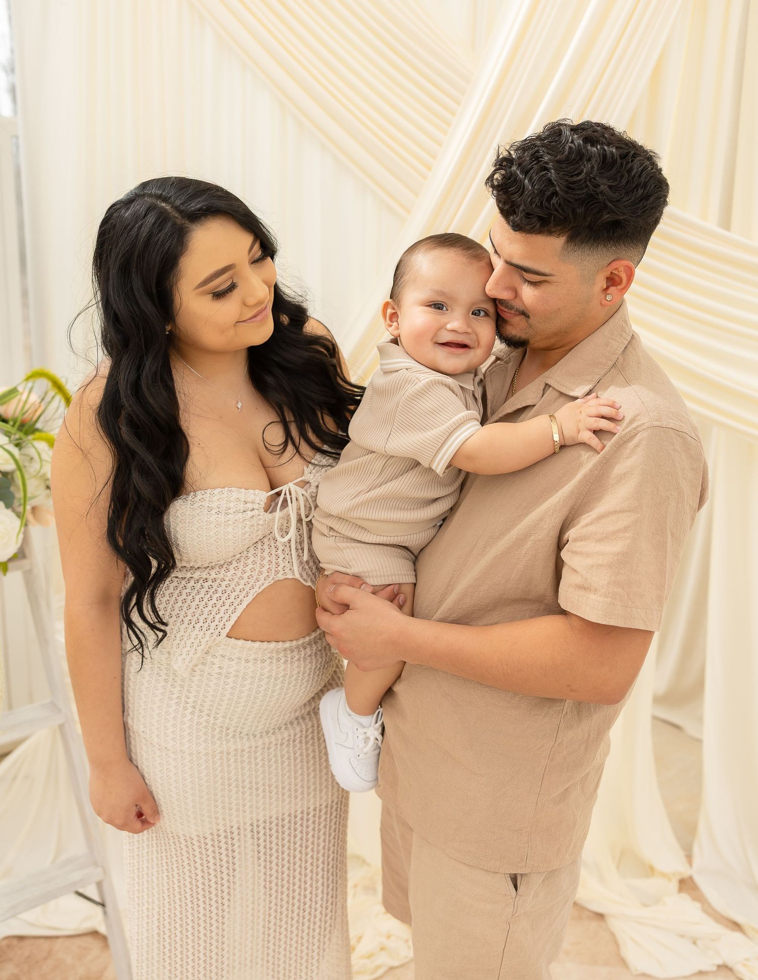 Family wearing neutral beige and cream outfits embraces lovingly in a series of intimate studio portraits.