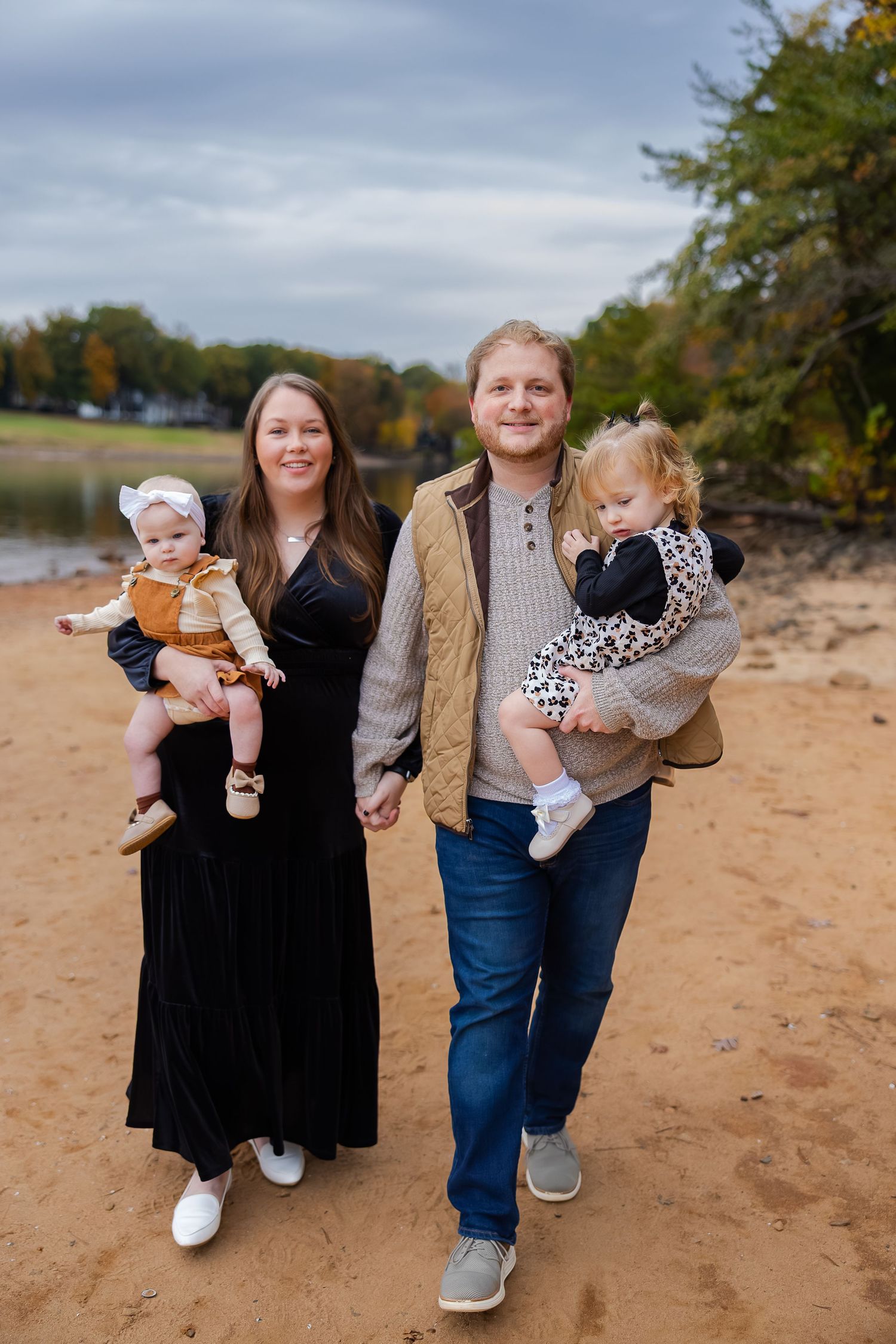 Family group standing together on sandy beach during autumn with trees in background.