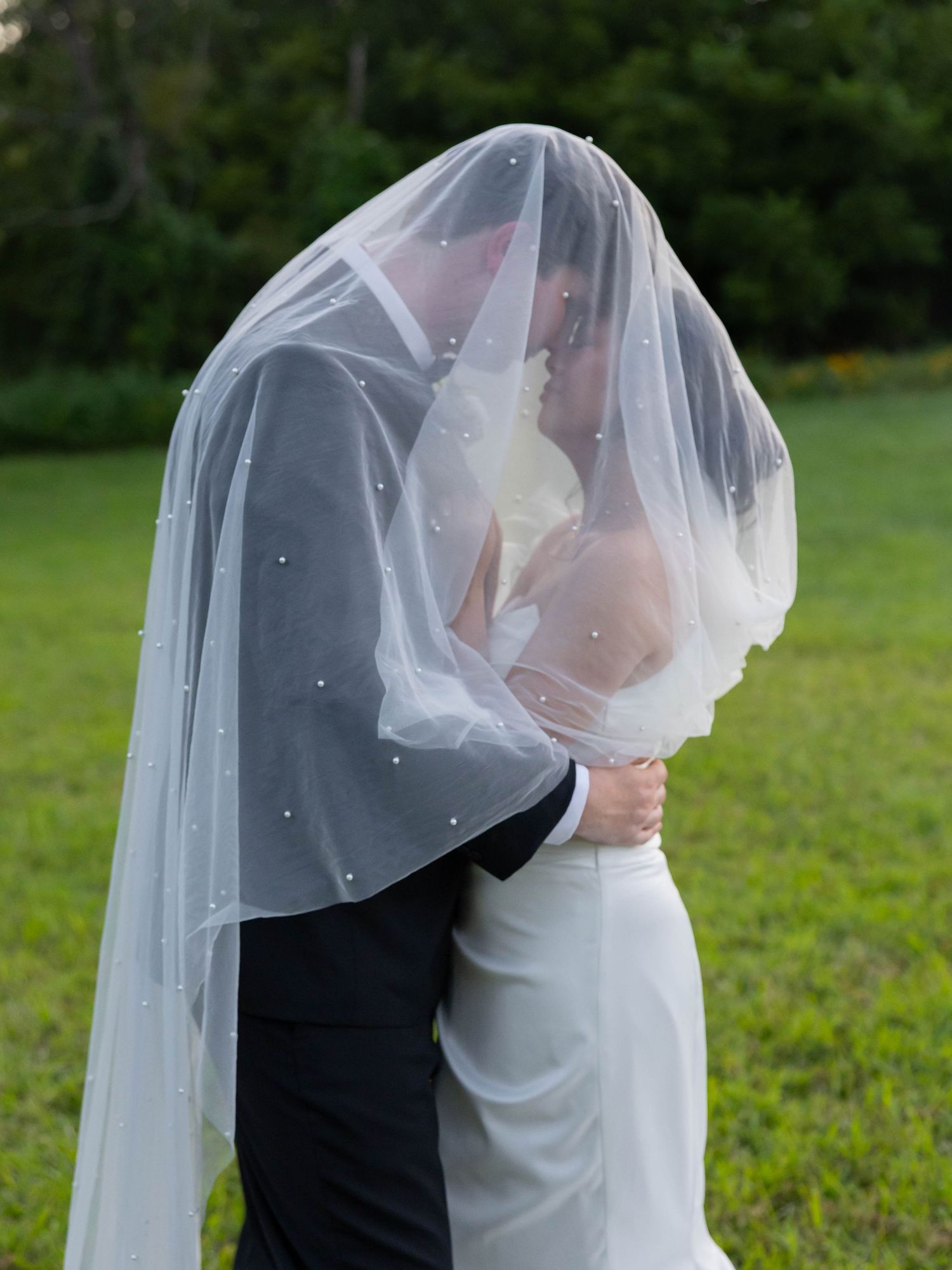 A romantic wedding moment captured as the couple shares a kiss under a flowing white veil in a garden setting.