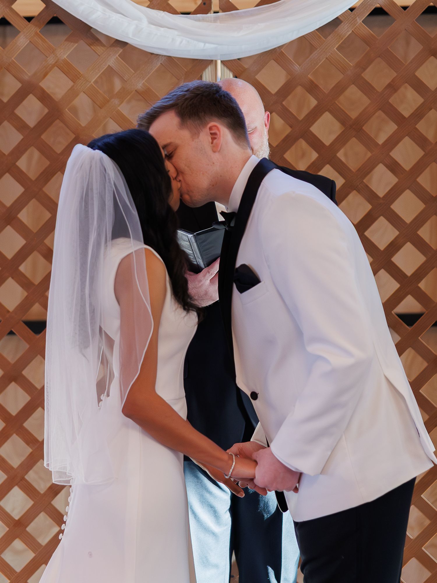A couple shares a tender moment during their wedding ceremony against a wooden lattice backdrop.