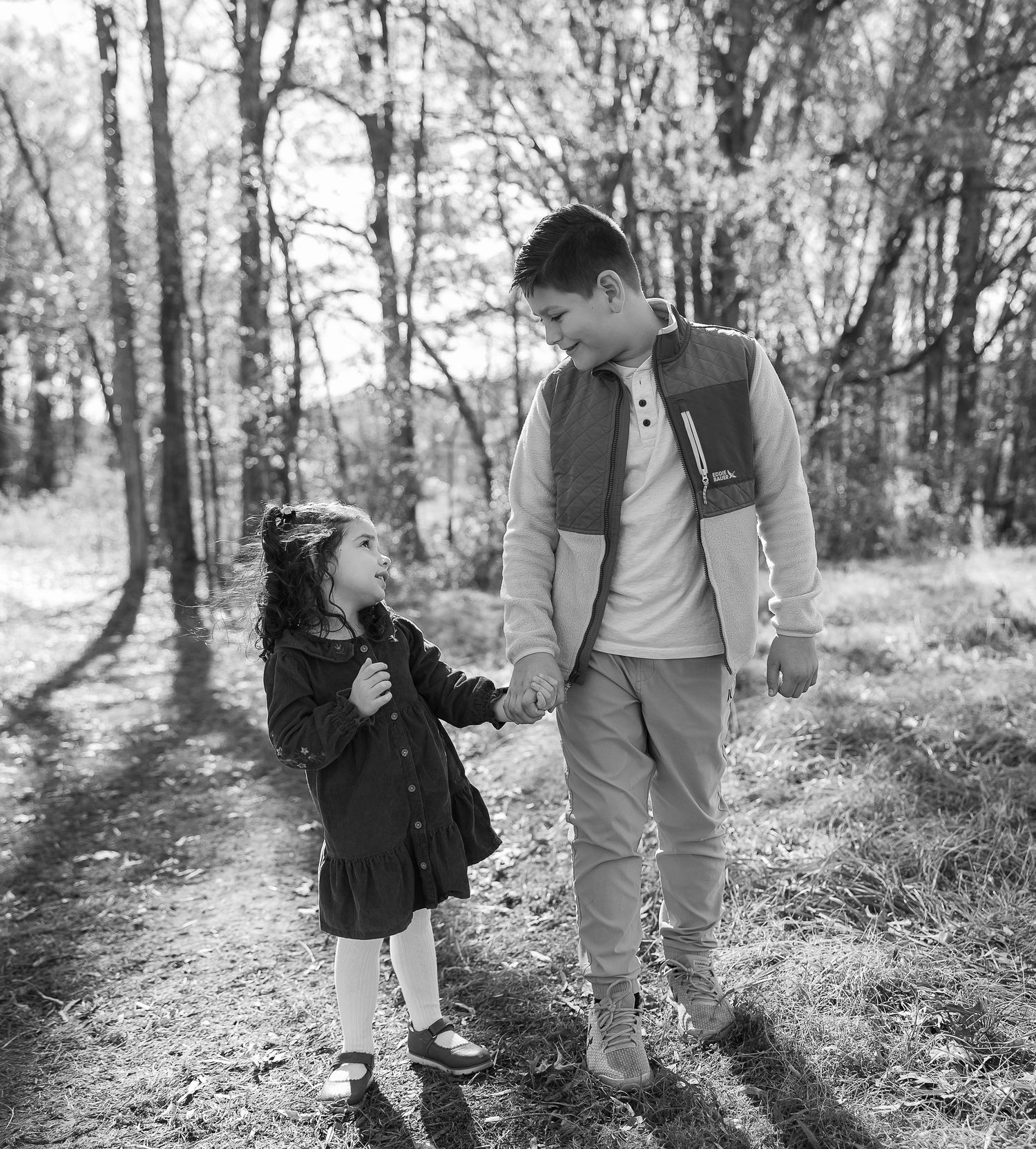 A heartwarming black and white photo of an adult and child sharing a tender moment together in a sunlit forest.