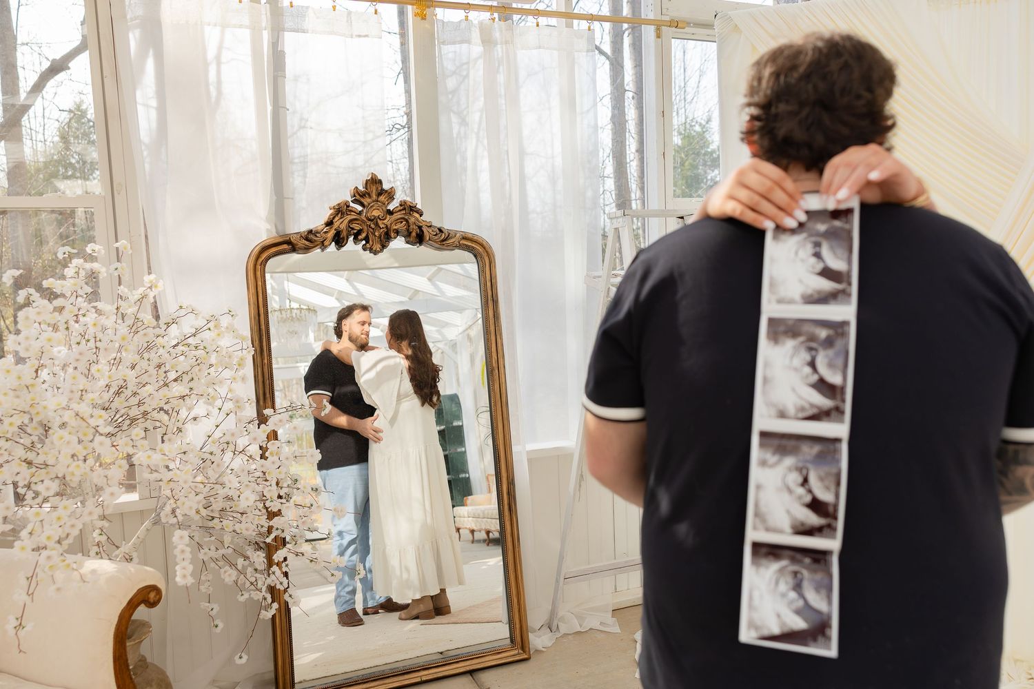 Ornate gold framed mirror being hung on a white wall while someone adjusts its placement.