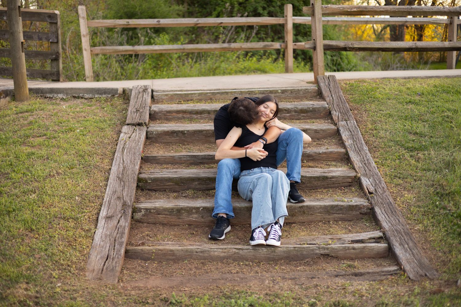 Someone sits in contemplative pose on weathered wooden steps along a nature path bordered by green grass.