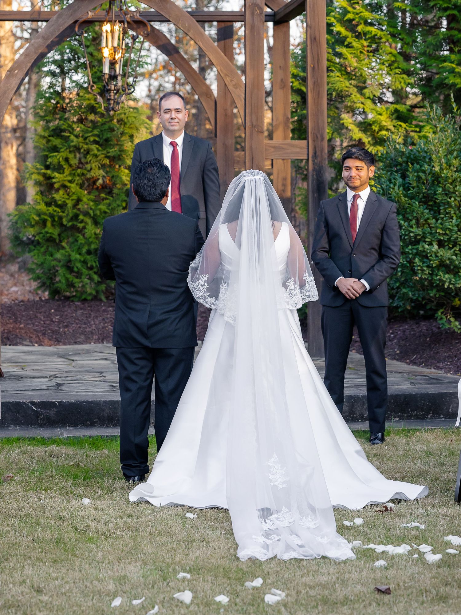 Bride walking down aisle in white gown and veil toward groom at outdoor wedding ceremony.