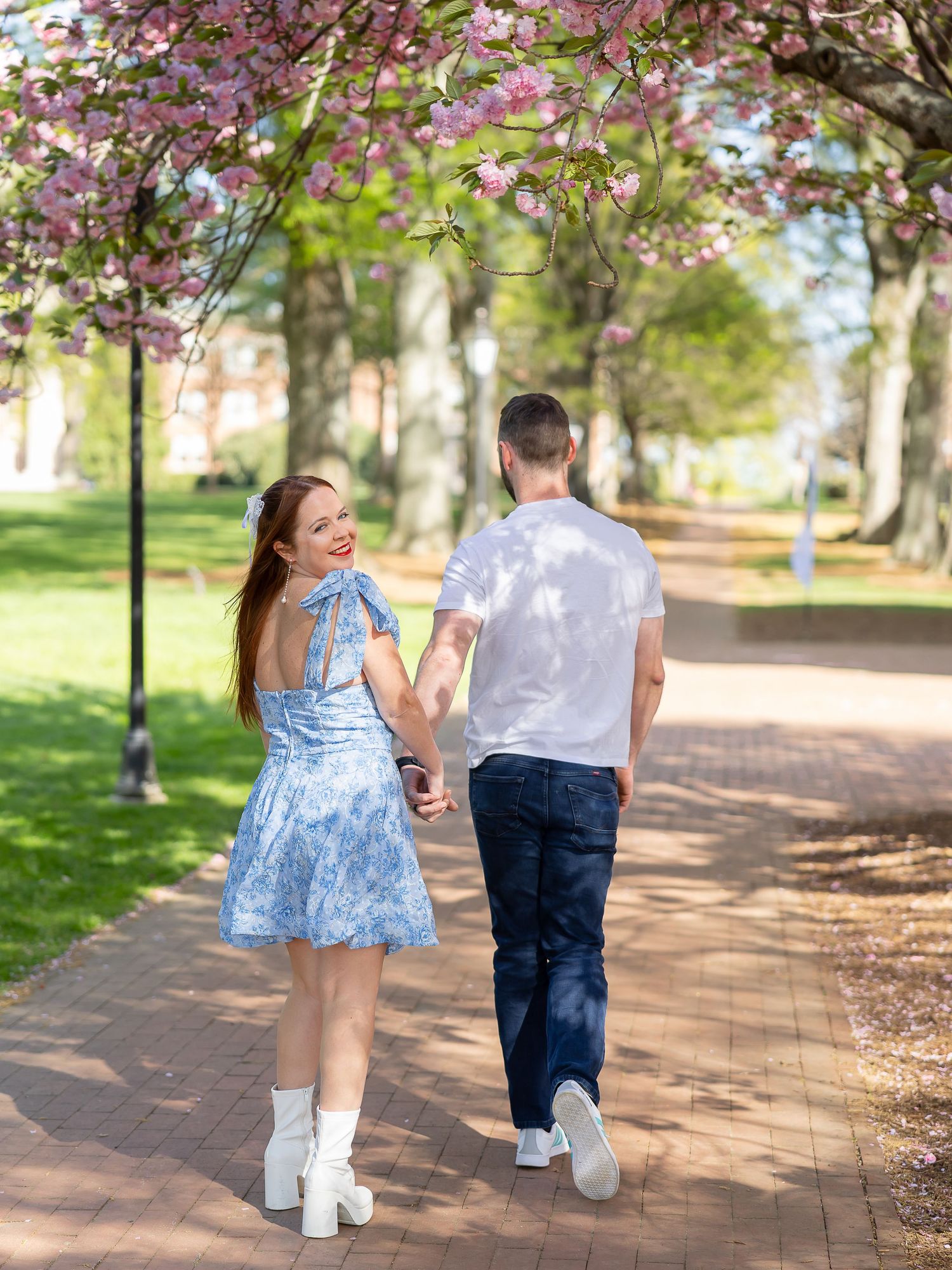 A young couple walking together in a park with blooming cherry blossom trees in the background.