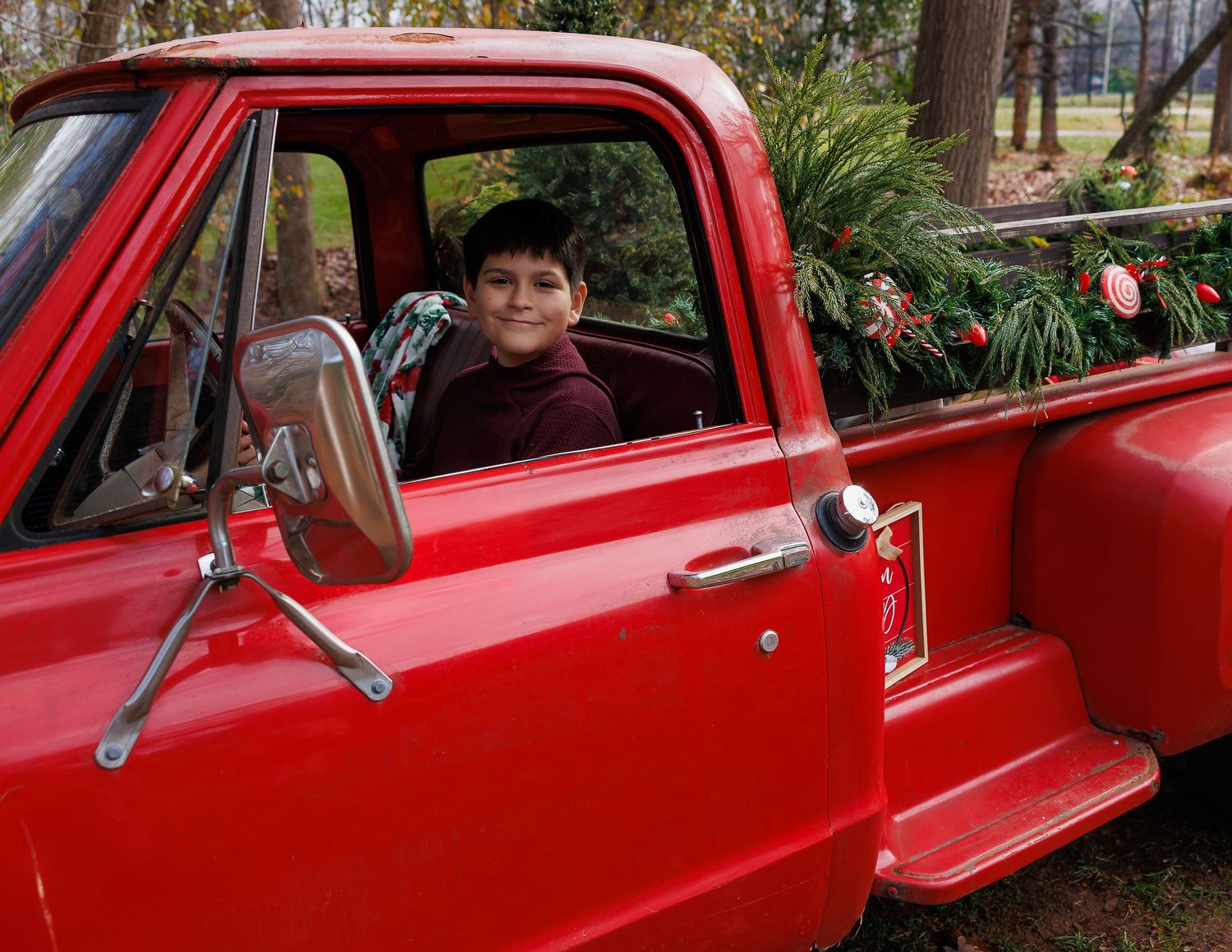 A classic red vintage pickup truck parked outdoors during the holiday season.