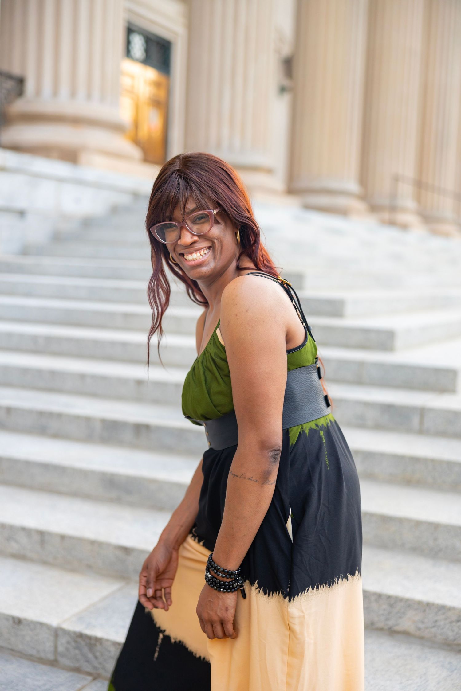 A person wearing a black and yellow colorblock dress stands smiling by stone columns at an elegant venue.